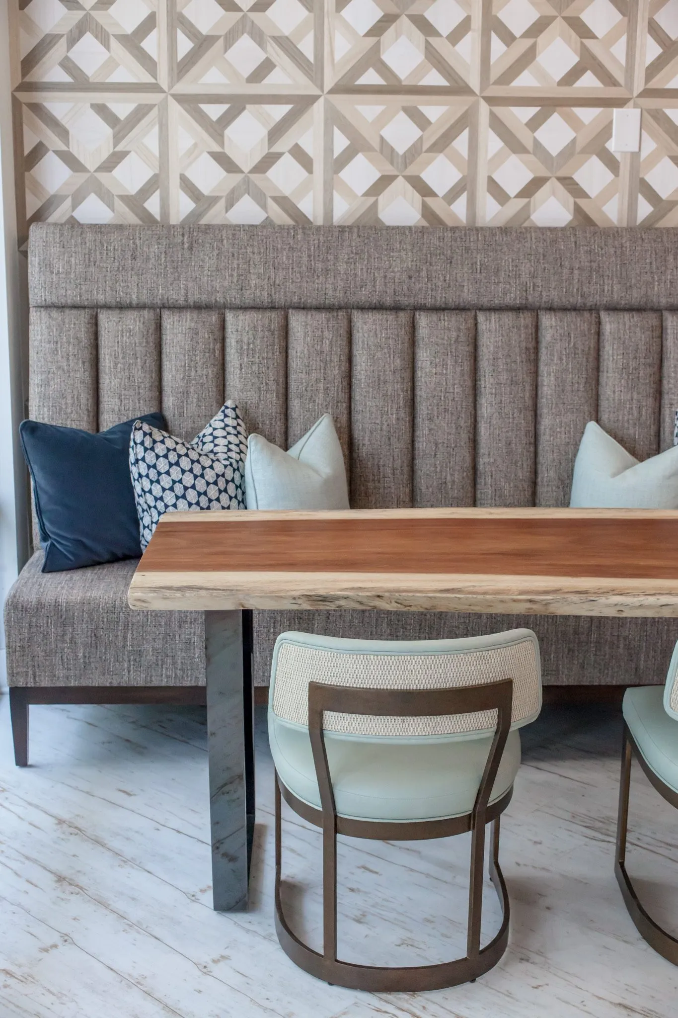 Multifamily interior detail: channel tufted banquette with pillows at a live edge table and sage chair
