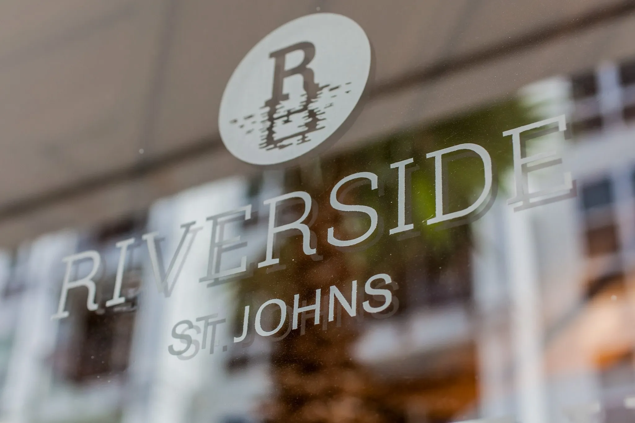 Multifamily community exterior: glass door decal with the community name and an R monogram, the street reflected behind