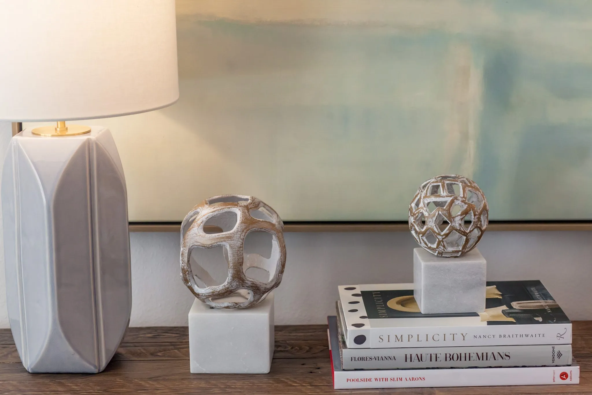 Multifamily interior detail: ceramic lamp, open metal orb sculptures on marble blocks and stacked books below a painting
