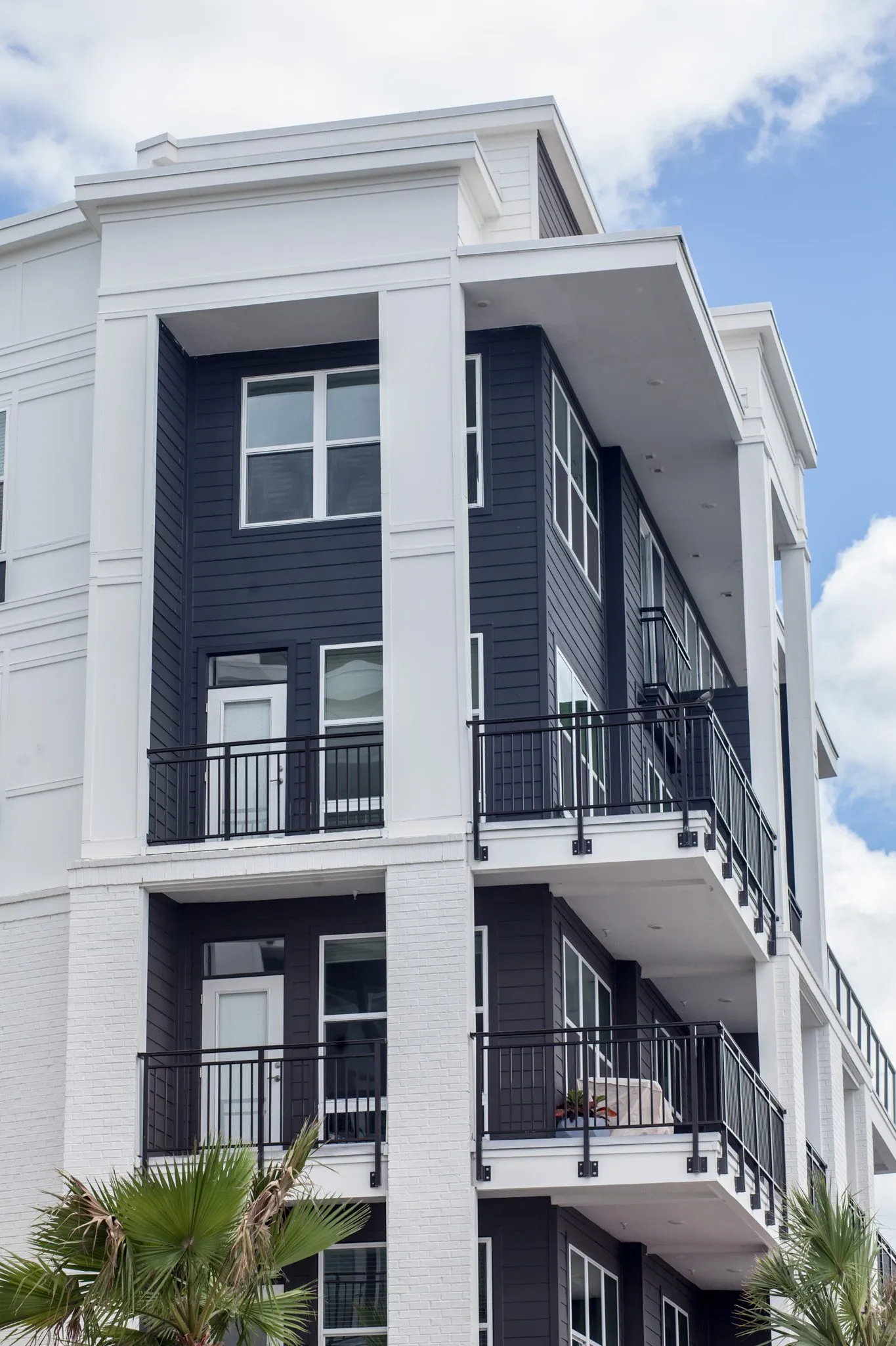 Multifamily community exterior: building corner with navy siding, black balcony railings and white columns, blue sky