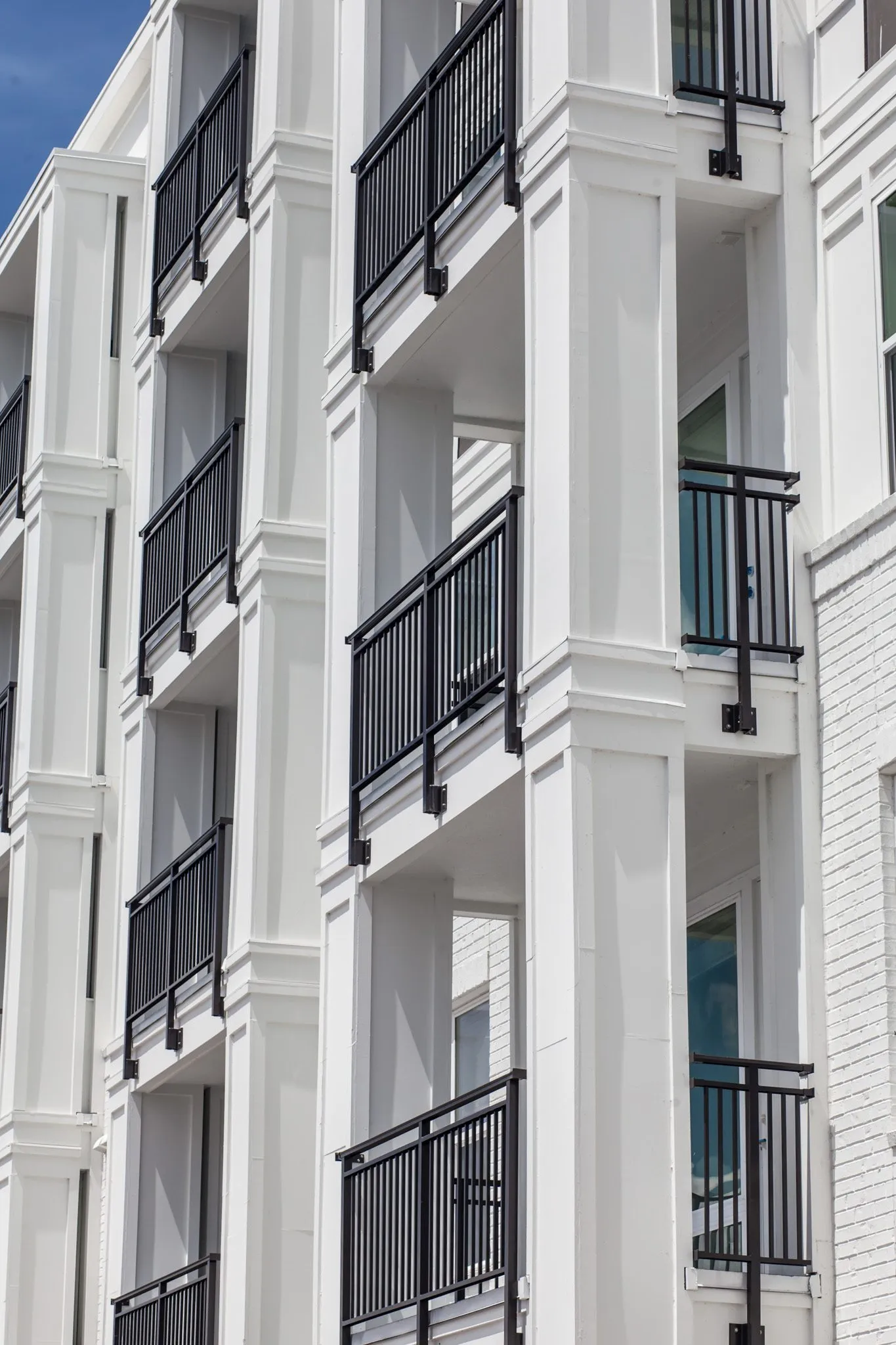 Multifamily community exterior: looking up a column of stacked black railed balconies on a white facade