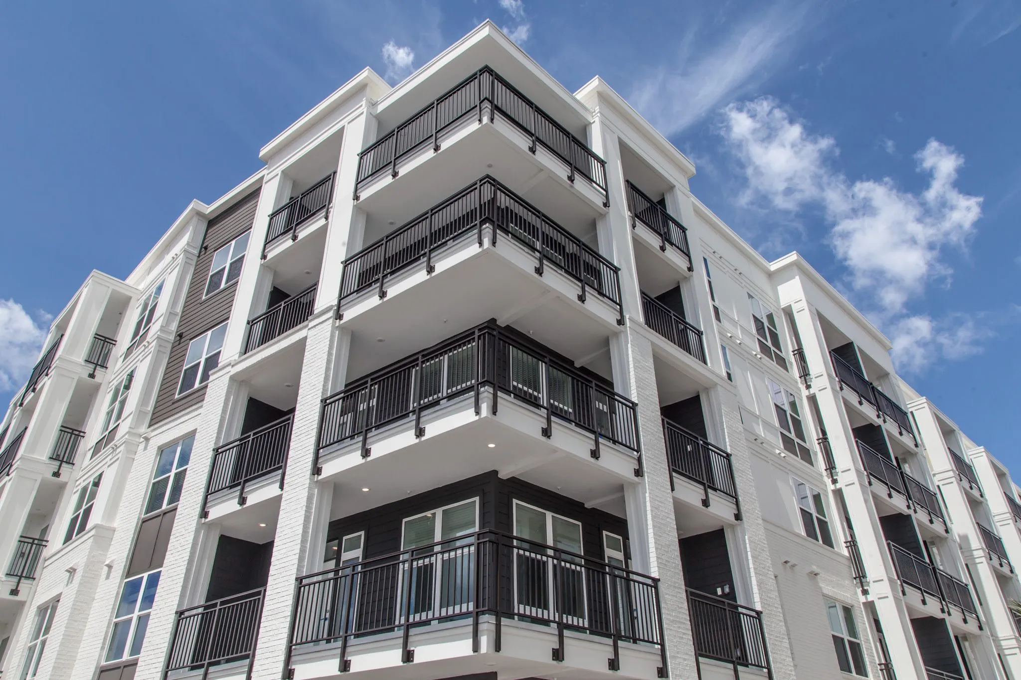 Multifamily community exterior: low view of a building corner with curved black railed balconies against a blue sky