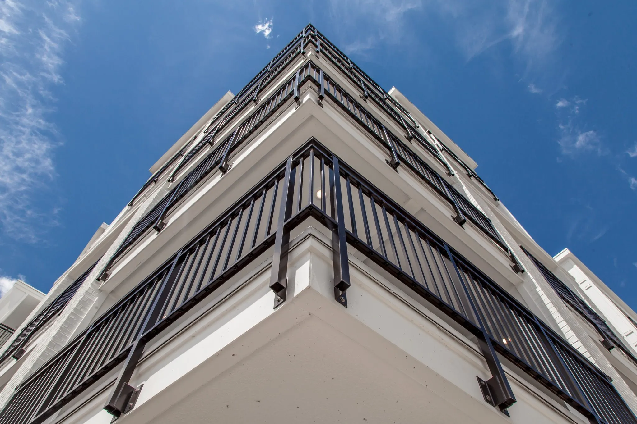 Multifamily community exterior: looking up a building corner at stacked balconies with black vertical railings