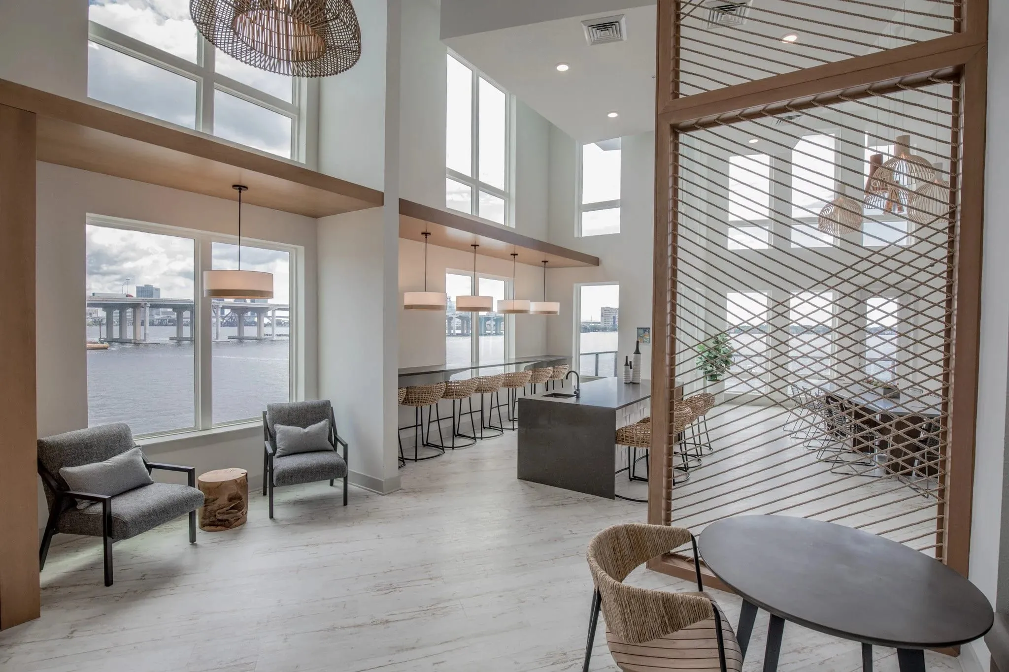 Multifamily amenity bar lounge with lounge chairs beside the wood and cord screen, the river through the windows