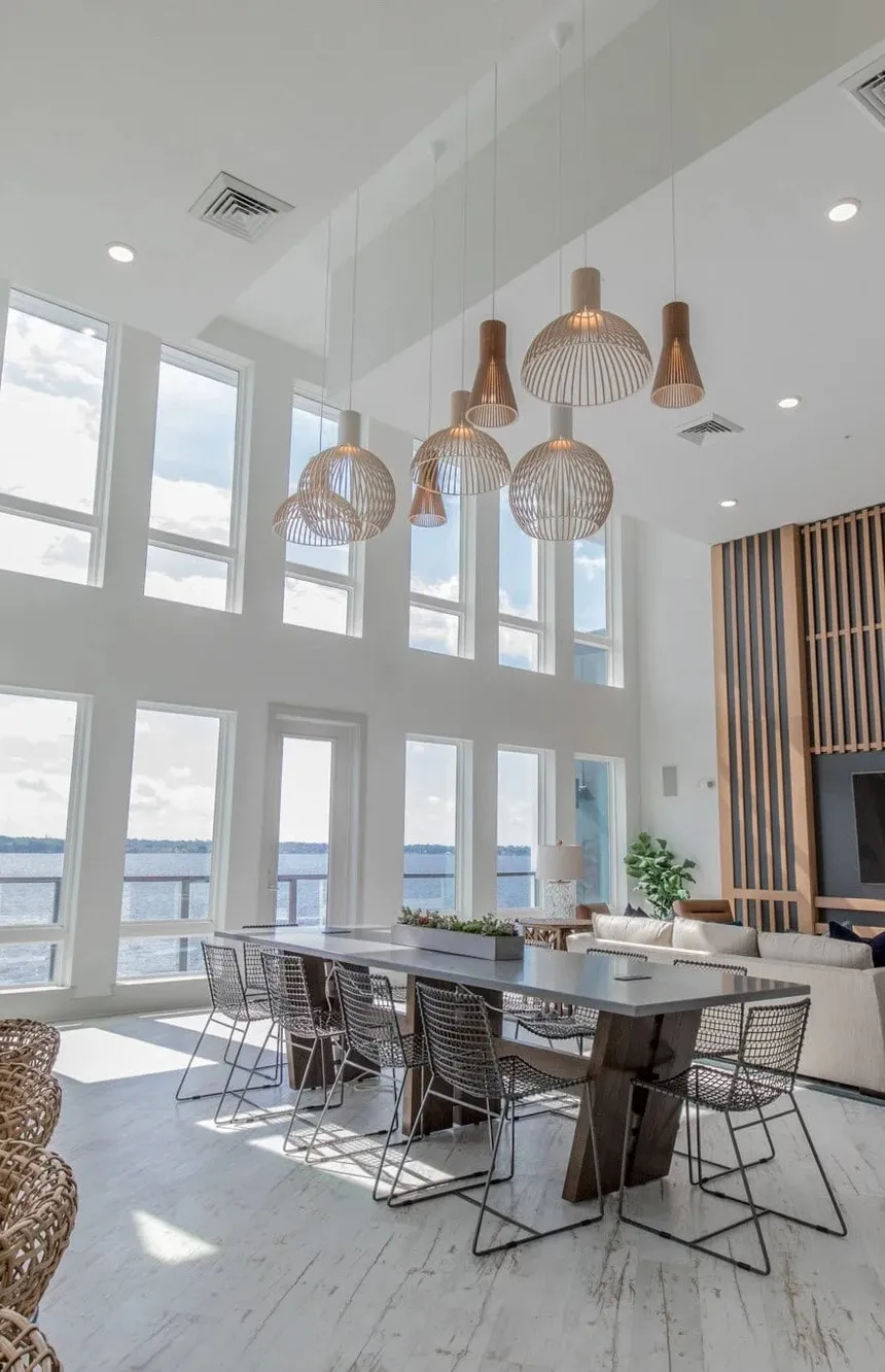 Multifamily double height clubroom with wood slat pendants over a long table, interior design by Banko Design at Riverside St. Johns, Jacksonville, Florida