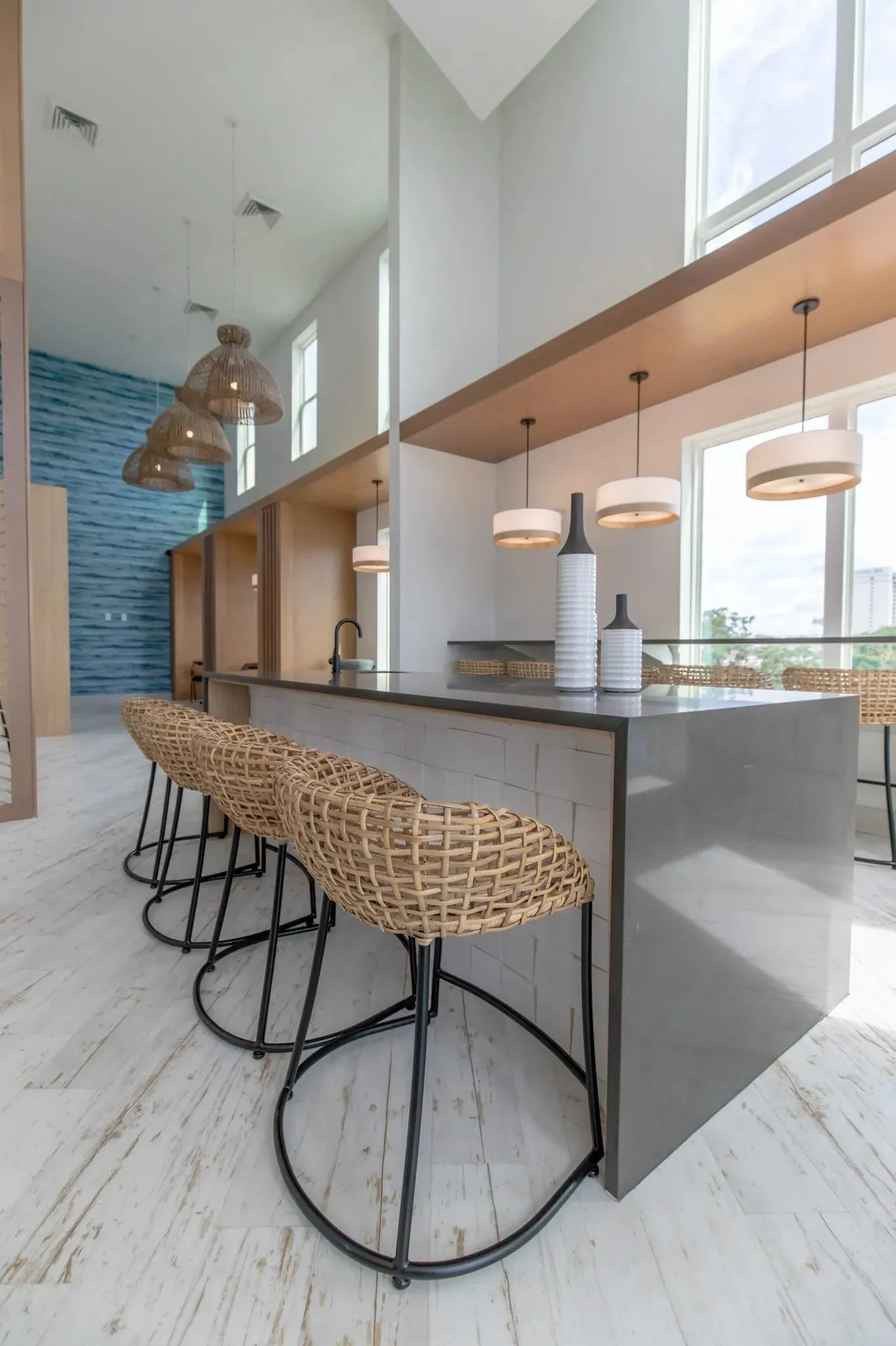 Multifamily amenity kitchen island with woven stools, drum pendants over the window bar and the blue water wall beyond