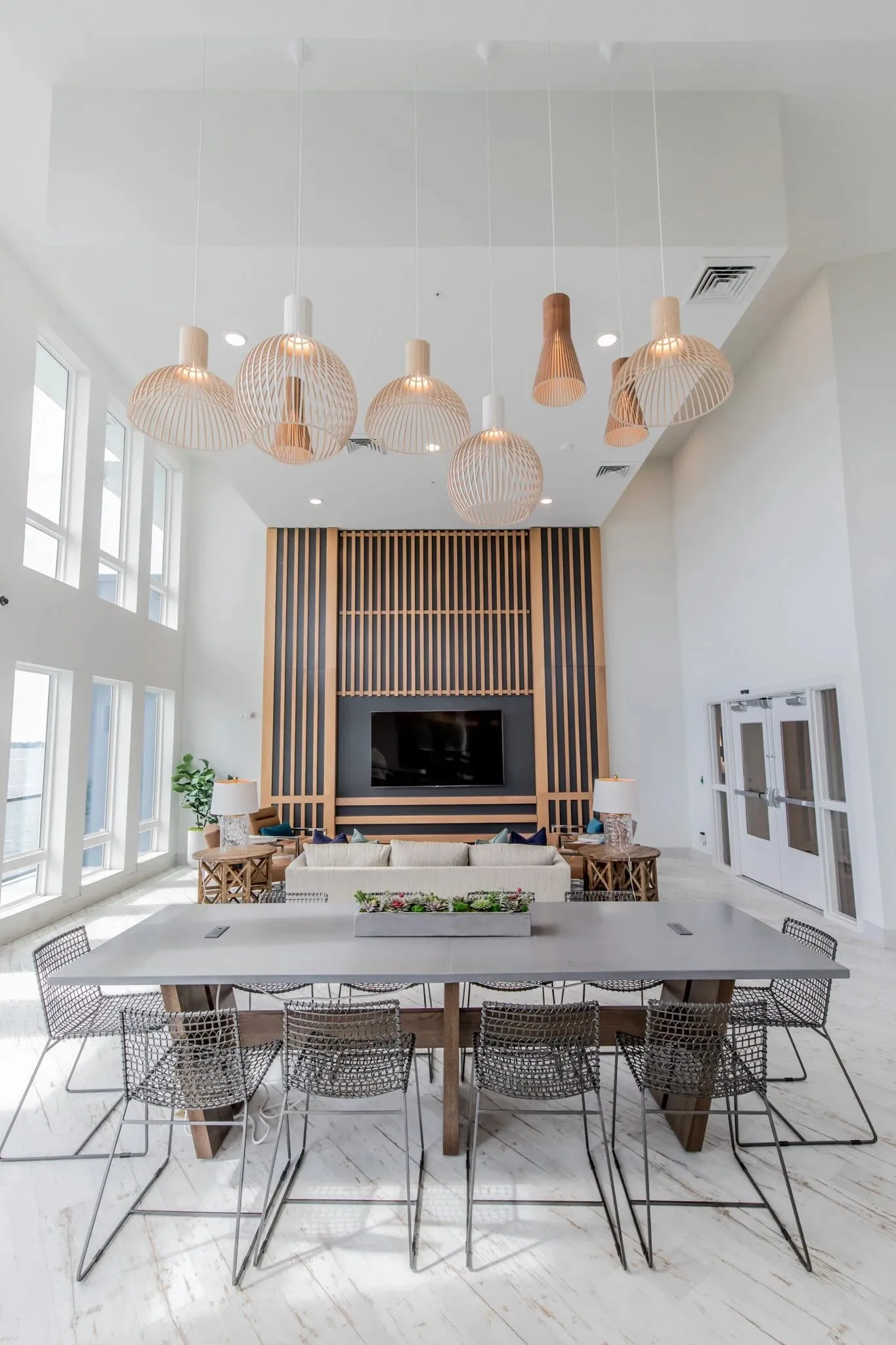Multifamily amenity communal table with wire chairs along its length under a cluster of woven pendants