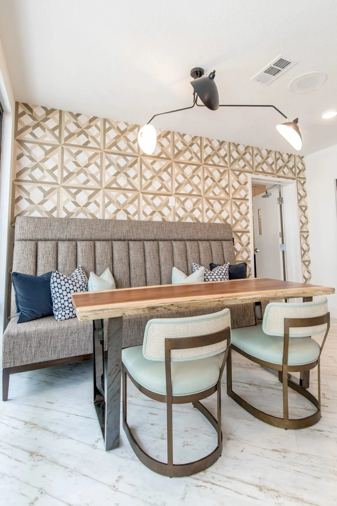 Multifamily dining nook with a channel-tufted banquette against geometric lattice wallcovering, a live edge table, two chairs