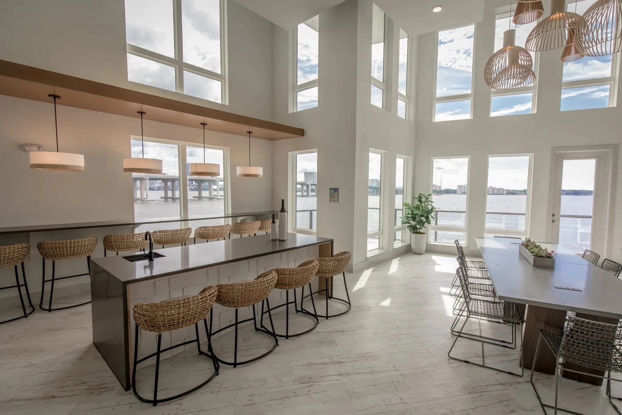 Multifamily amenity kitchen bar with woven stools along the island, the river through the two-story glazing