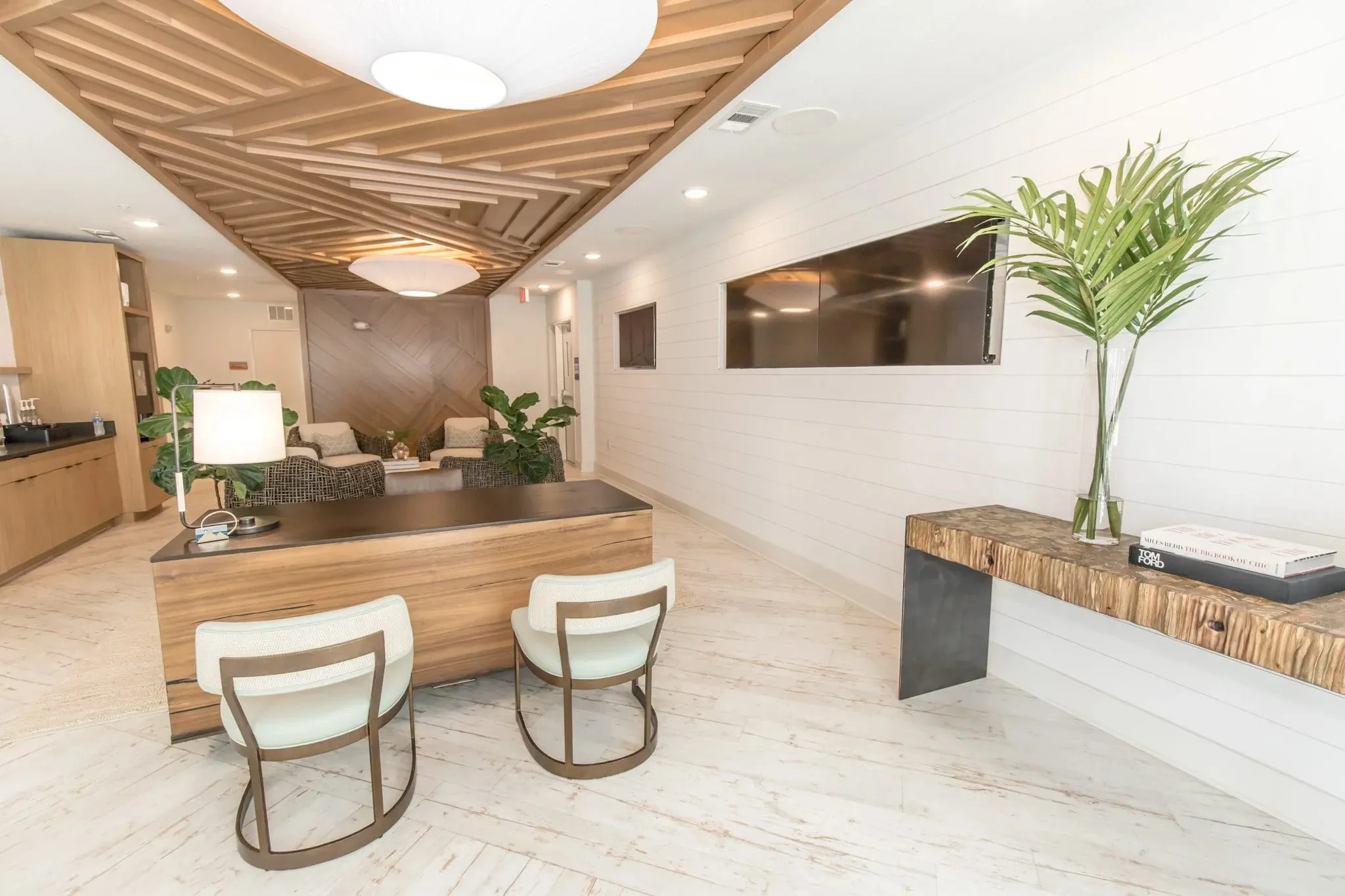 Multifamily amenity leasing desk with a timber slat ceiling feature above and two cream upholstered chairs in front