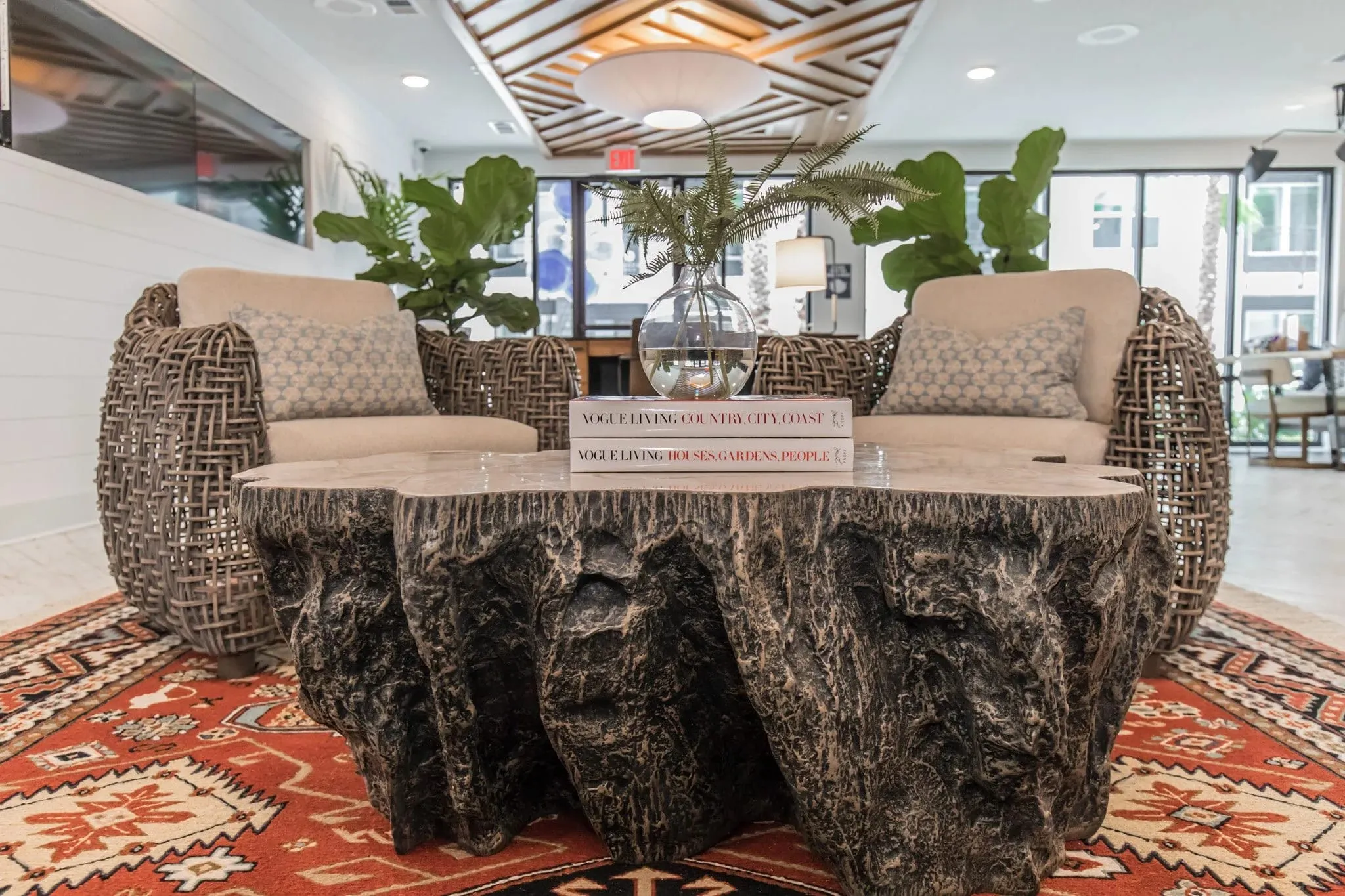 Multifamily amenity leasing lounge with woven barrel chairs around a dark tree stump table on a red kilim rug