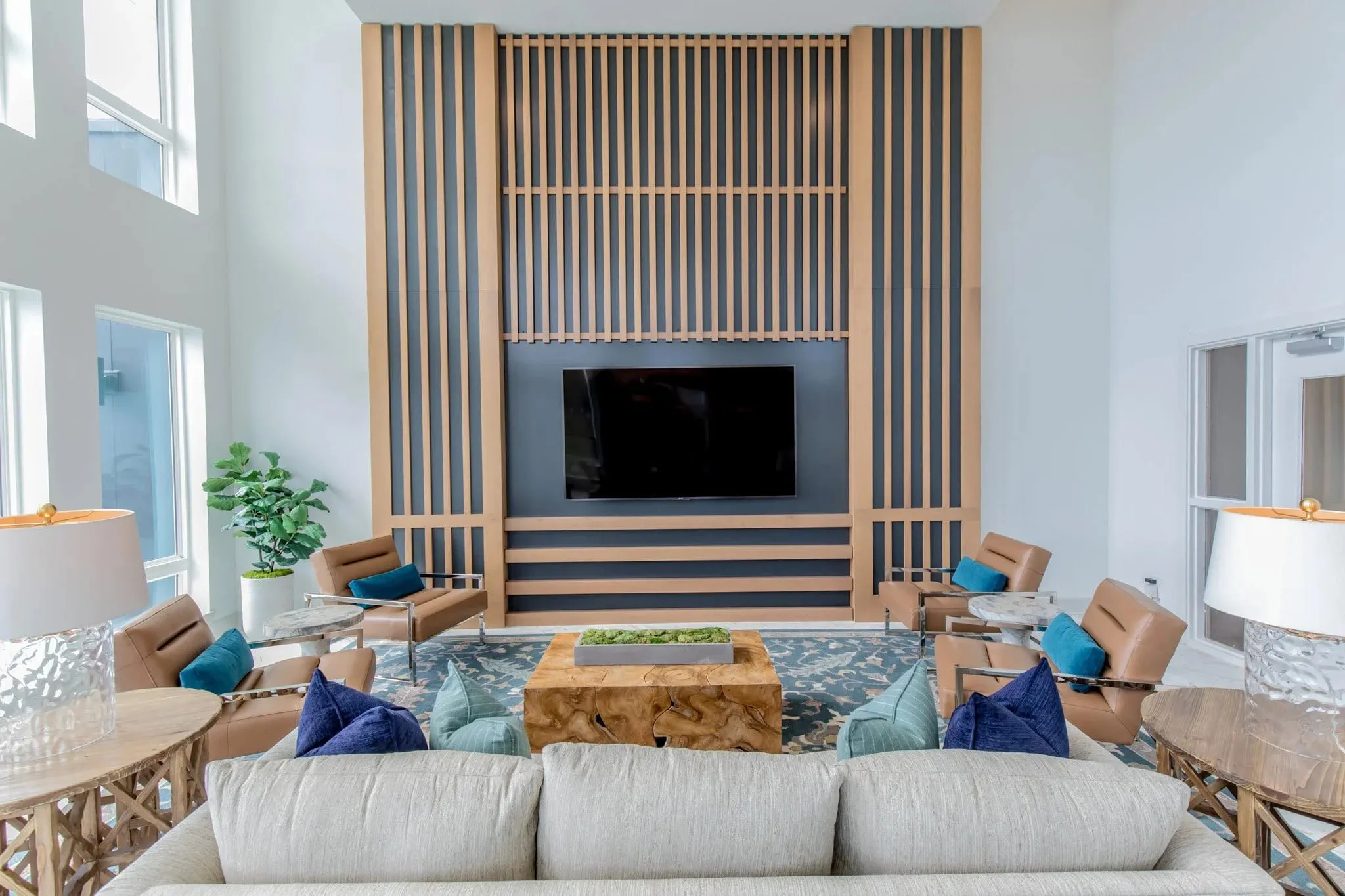 Multifamily amenity media lounge with a wood slat and navy wall around the television, tan sling chairs and a cream sofa