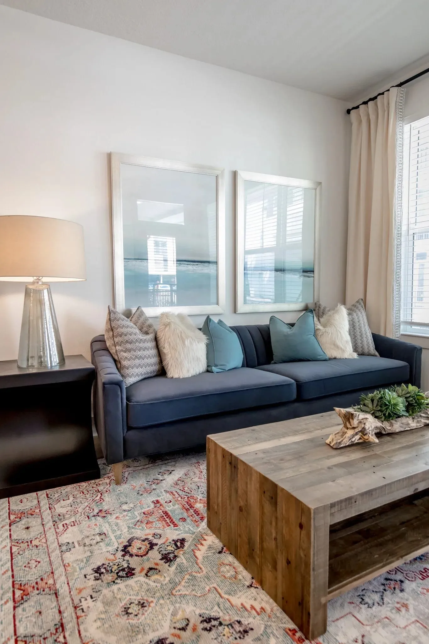 Multifamily sitting area with a navy sofa and a reclaimed wood coffee table on a patterned rug beside the window