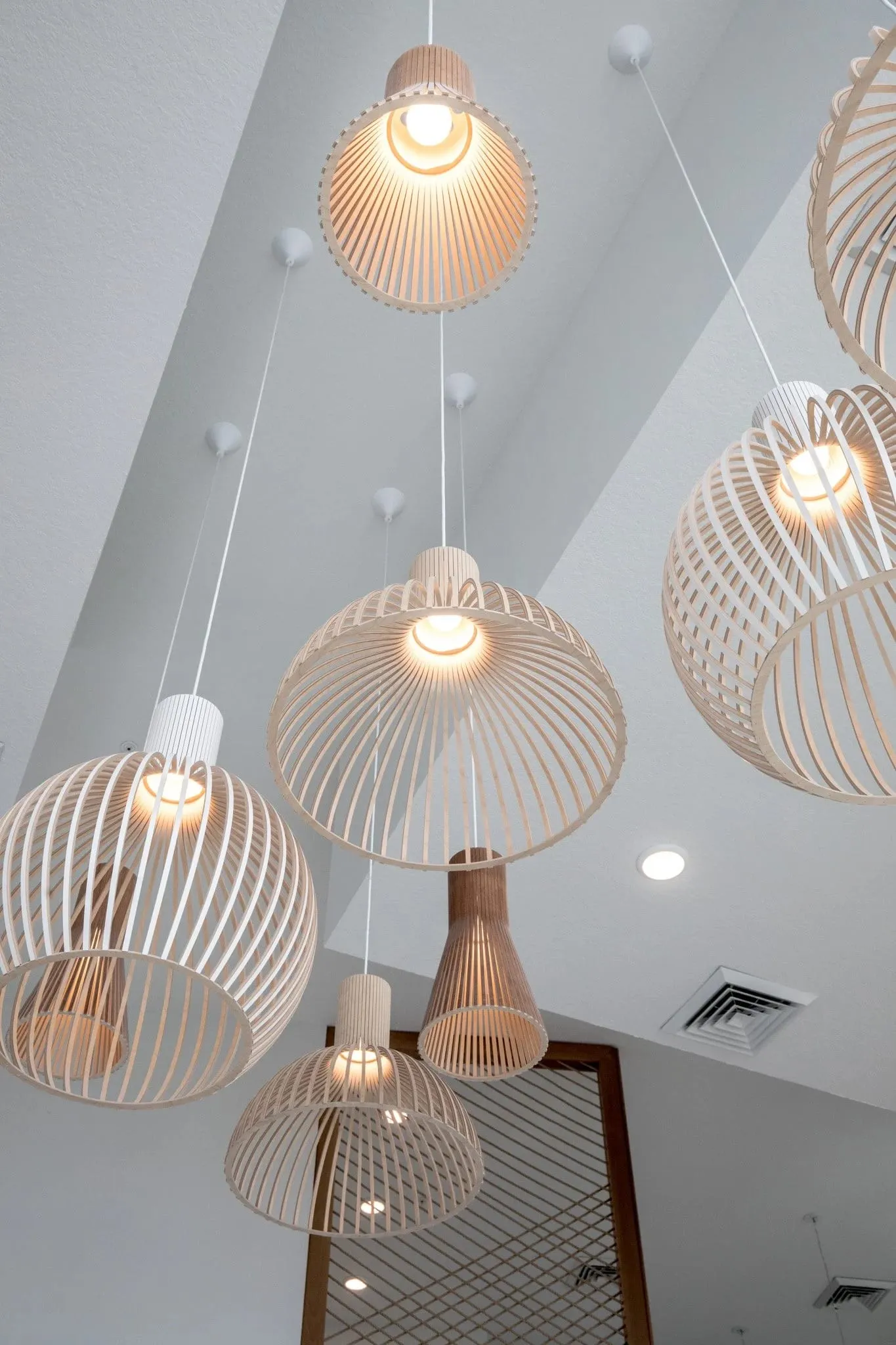 Multifamily interior detail: cluster of slatted wood pendant shades hung at different heights in the double-height space