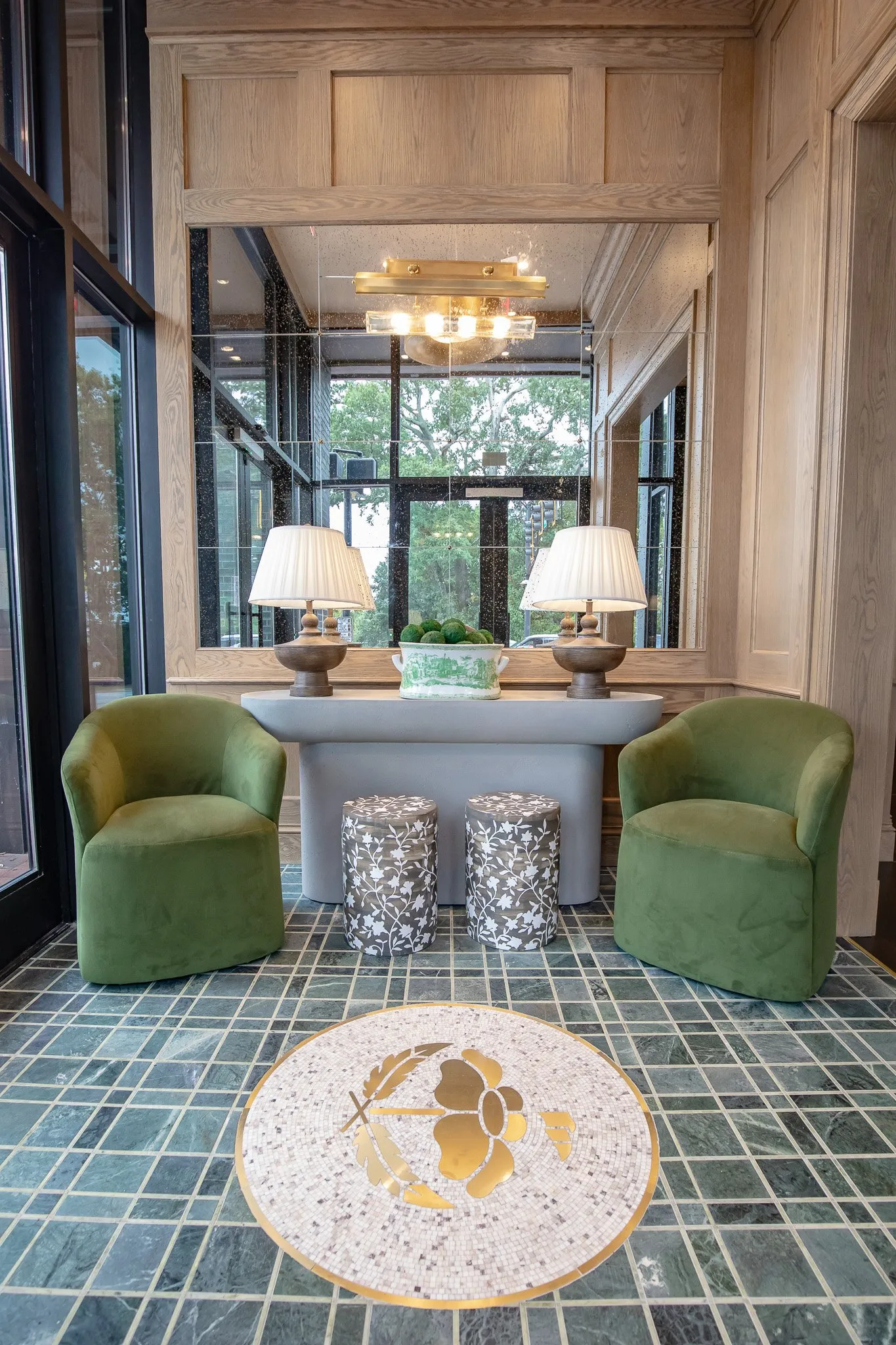 Private club entry foyer with an inlaid rose mosaic medallion in the green tile floor, velvet chairs at a stone console