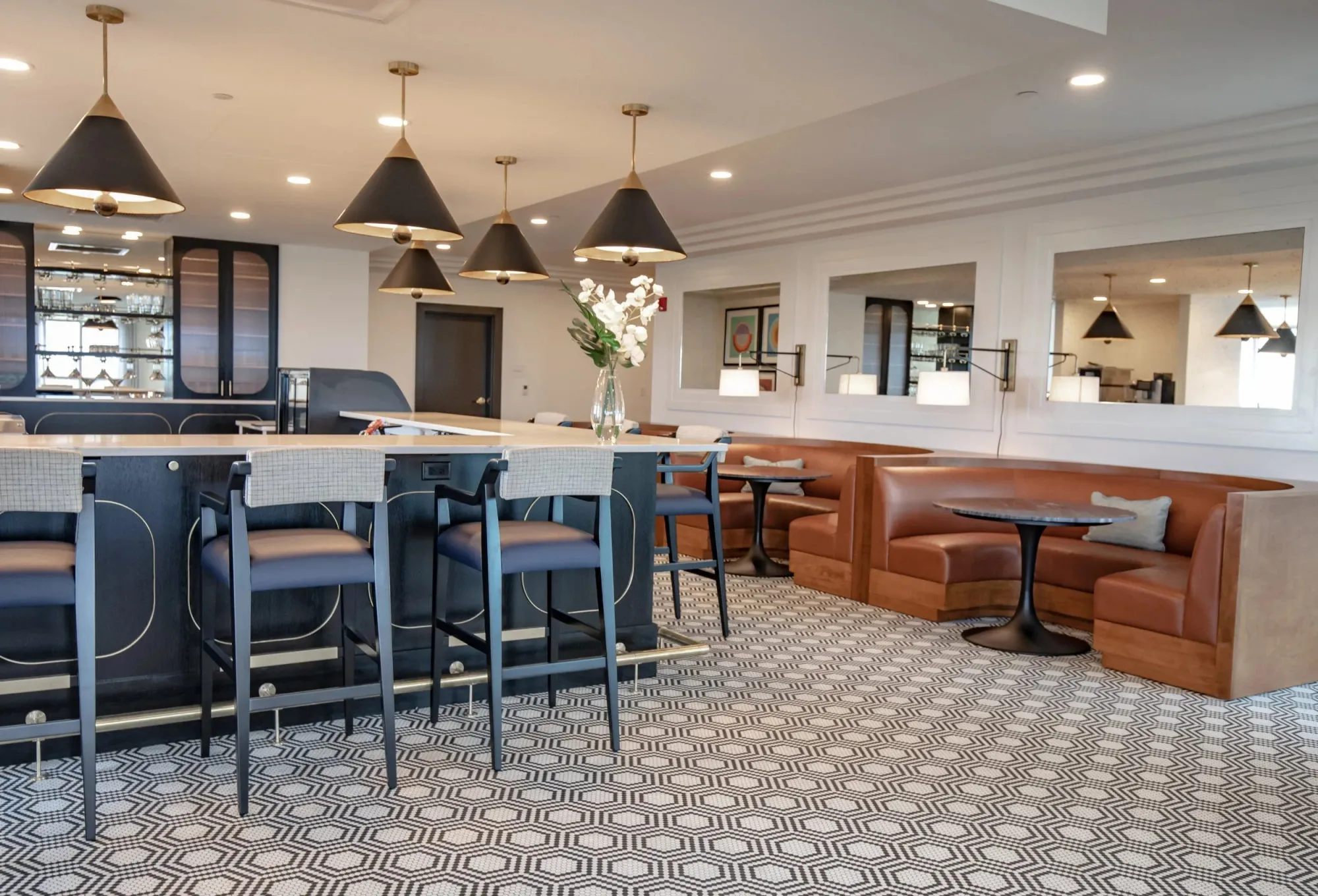 Senior living bar with black conical pendants over counter stools, cognac leather booths and patterned black and white carpet