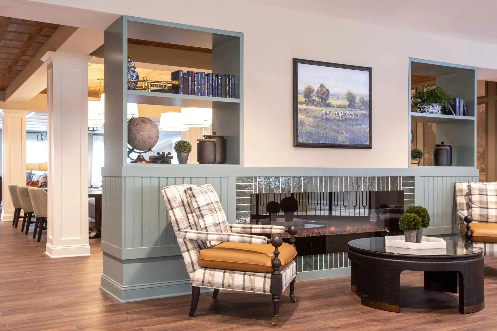 Senior living fireside seating with a plaid wing chair by a sage beadboard fireplace with a mirrored tile surround