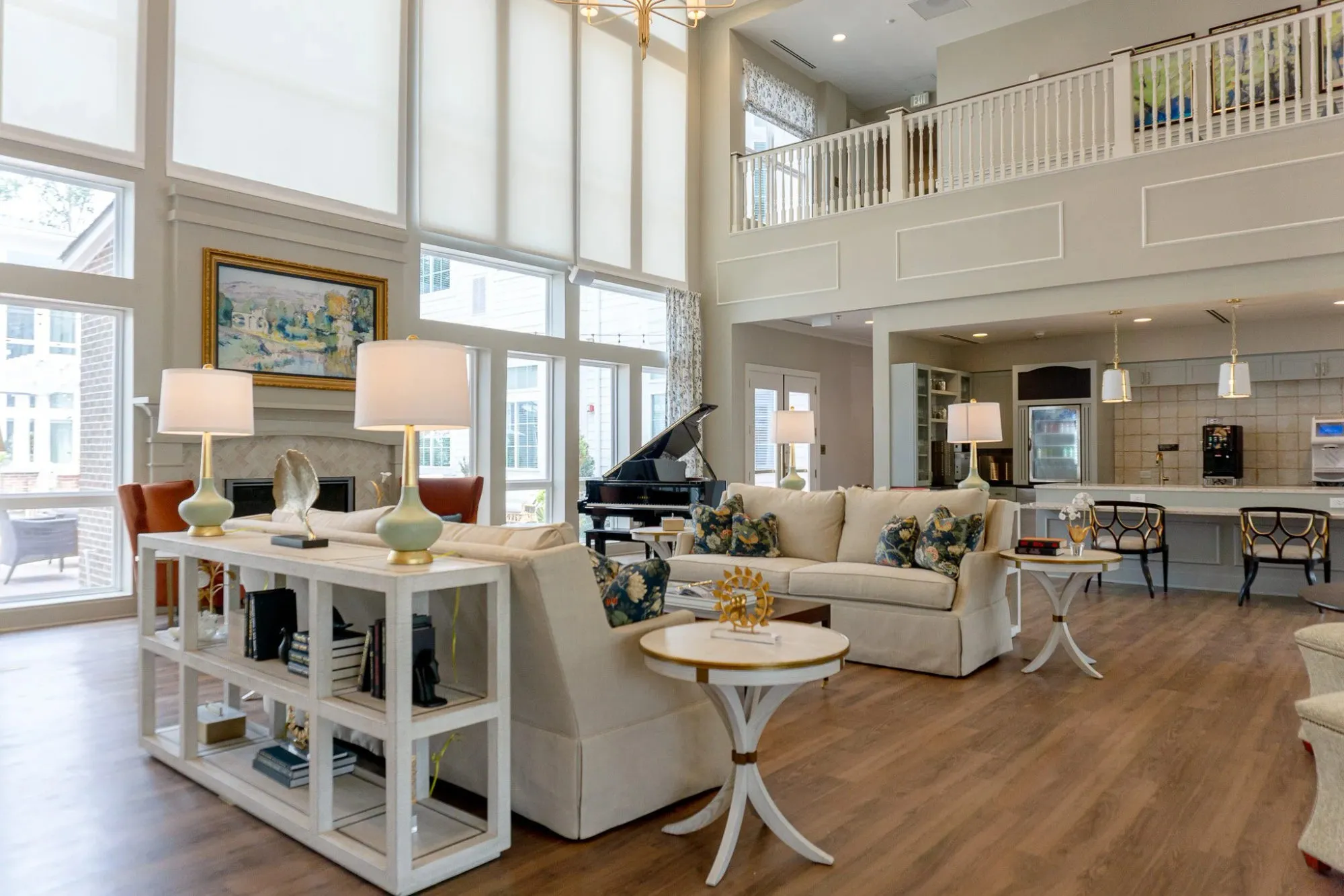 Senior living double-height great room with cream sofas, a grand piano and a landscape painting above the fireplace