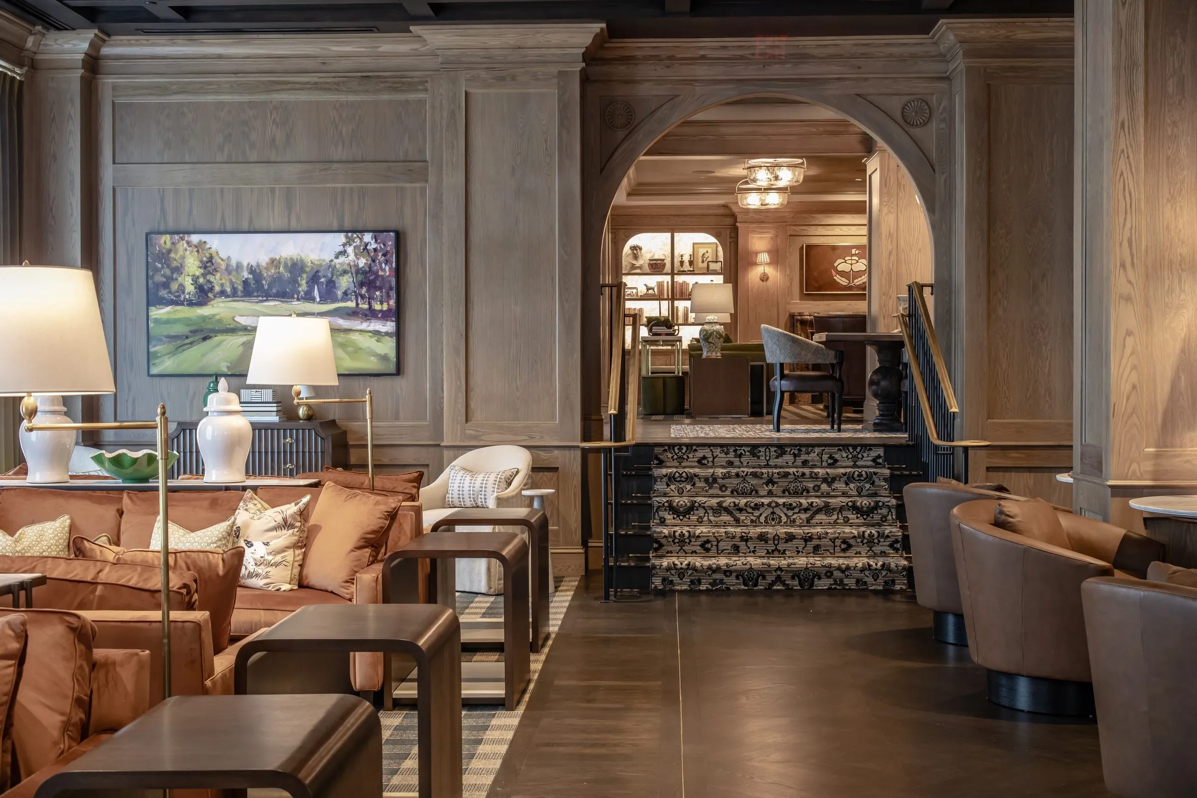 Oak-panelled club study with a marble fireplace, lit display shelves and a linen armchair on a tartan rug