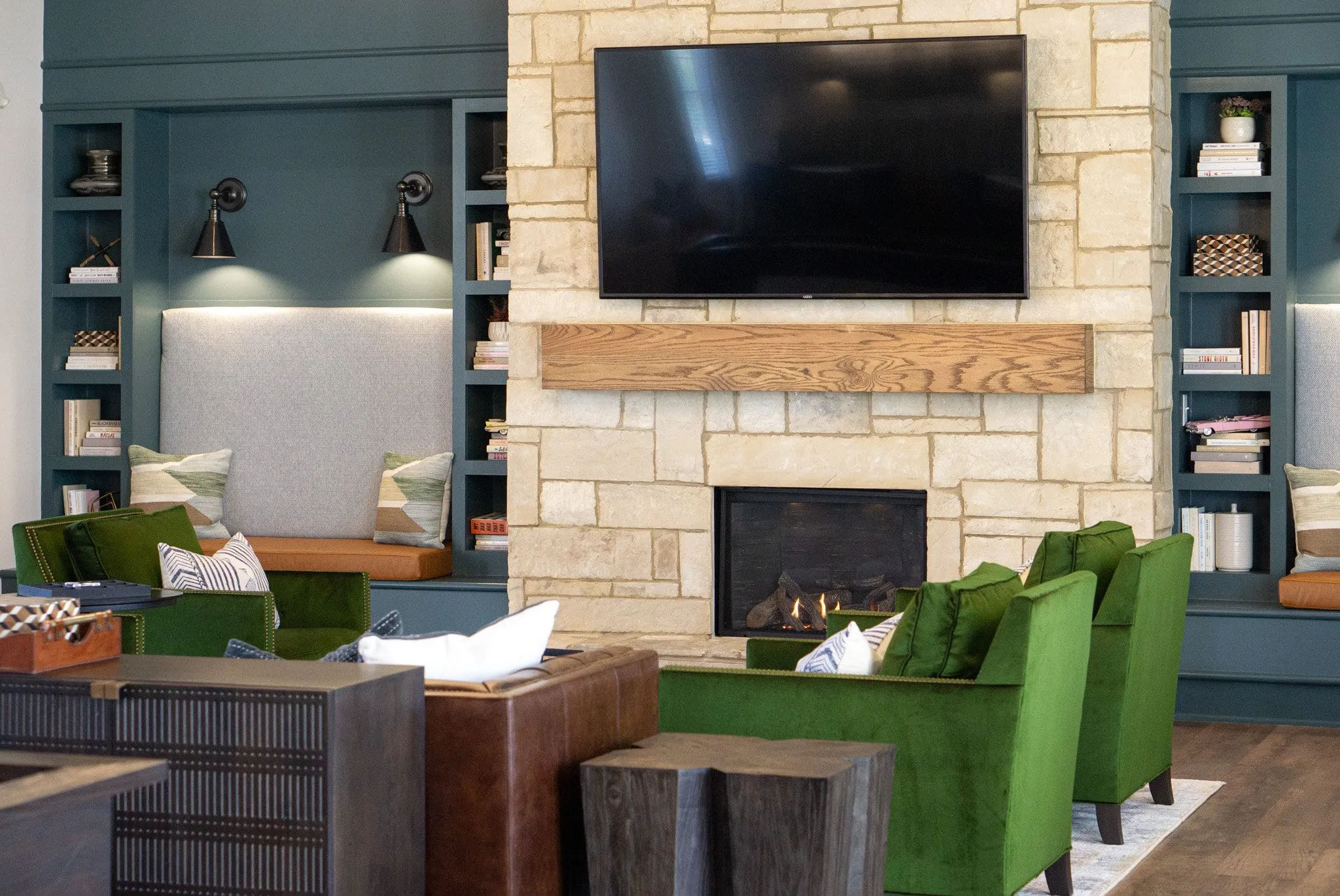 Multifamily amenity clubroom fireplace with a stone surround and teal built-ins flanking a reclaimed wood mantel