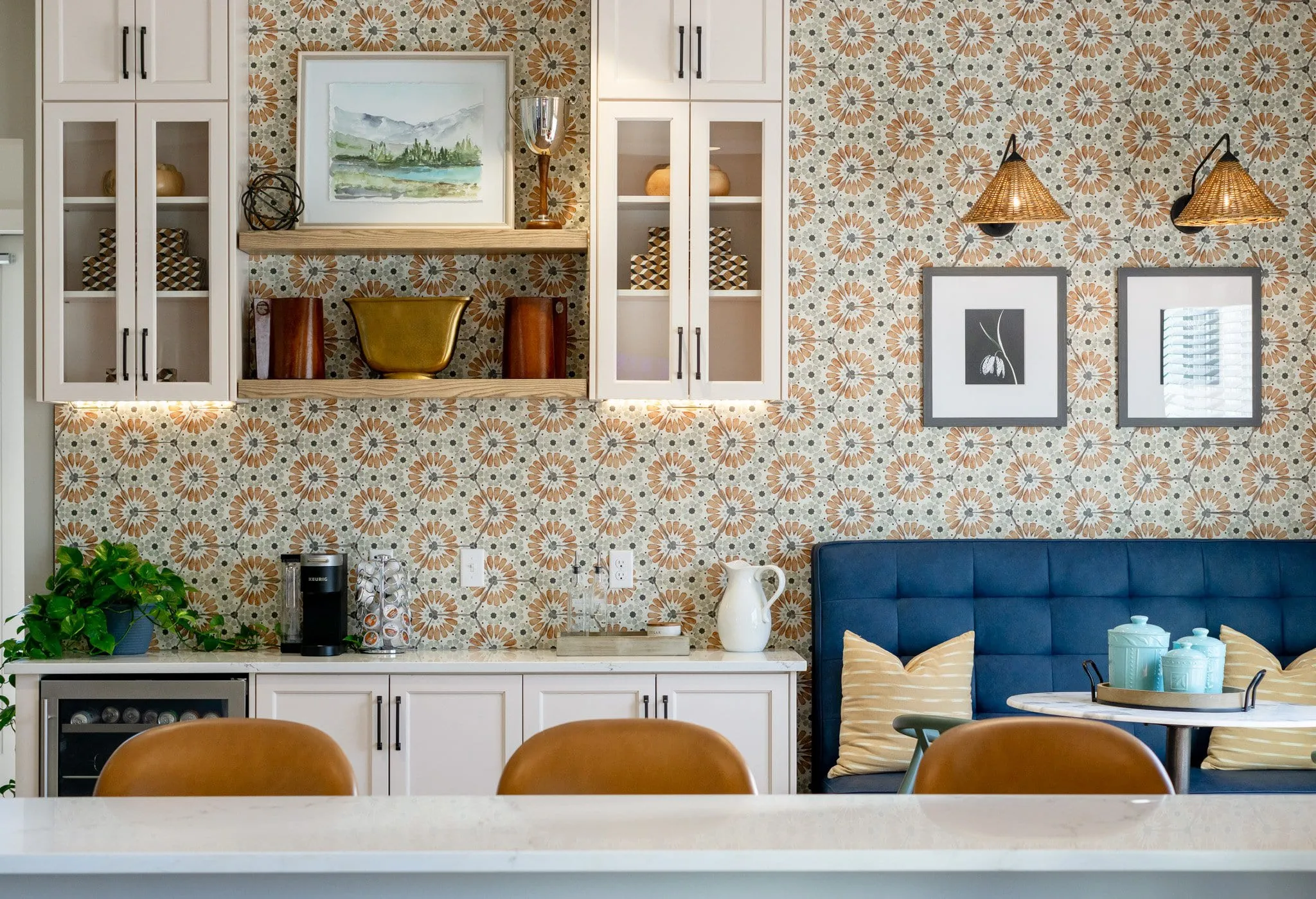 Multifamily amenity coffee bar with glass-front cabinets on patterned orange tile beside a blue tufted banquette