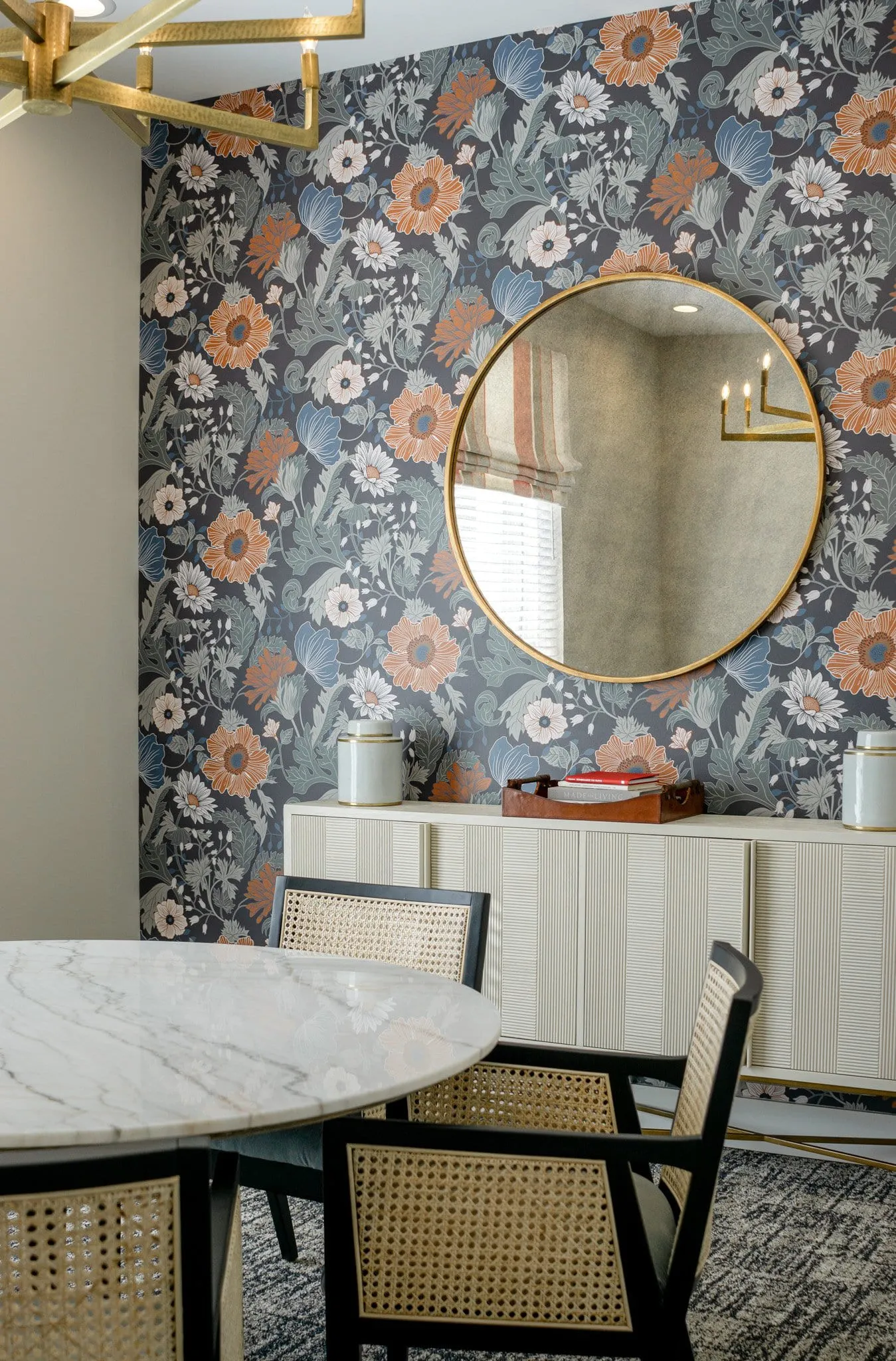 Multifamily amenity console vignette with a round brass mirror on floral wallcovering above a fluted cabinet