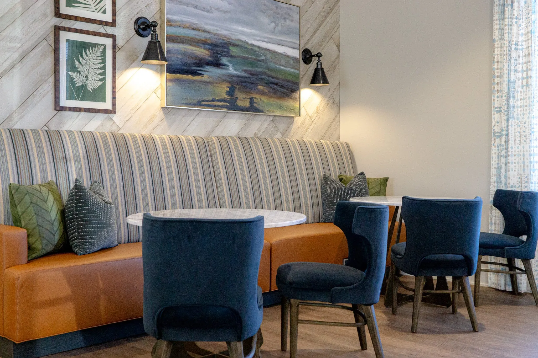 Multifamily amenity coworking banquette with a striped bench and blue chairs under wall sconces and framed art