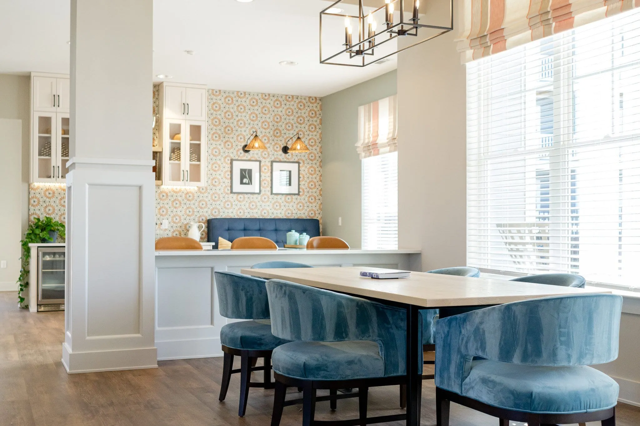 Multifamily amenity dining area with blue velvet chairs around a light wood table under a lantern chandelier
