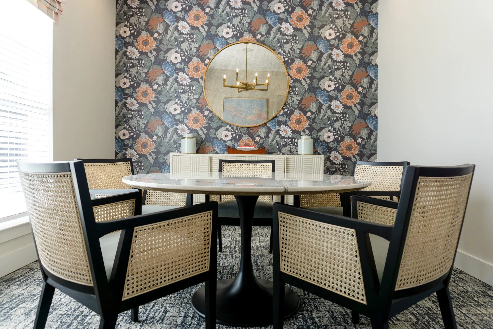 Multifamily amenity cafe table with cane and black wood chairs against a floral wallcovering below a brass mirror