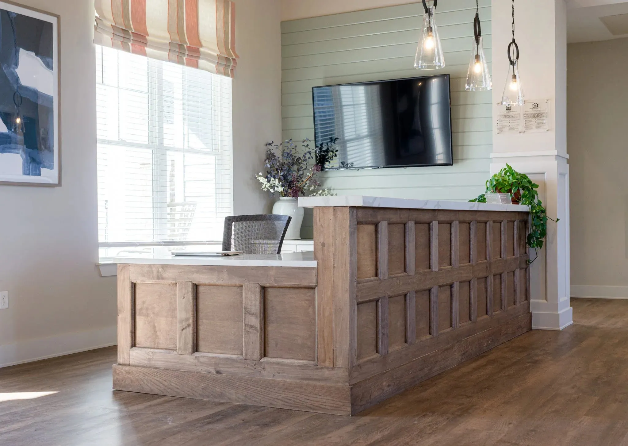 Multifamily amenity leasing desk with paneled oak millwork below a mounted screen and pendant lights