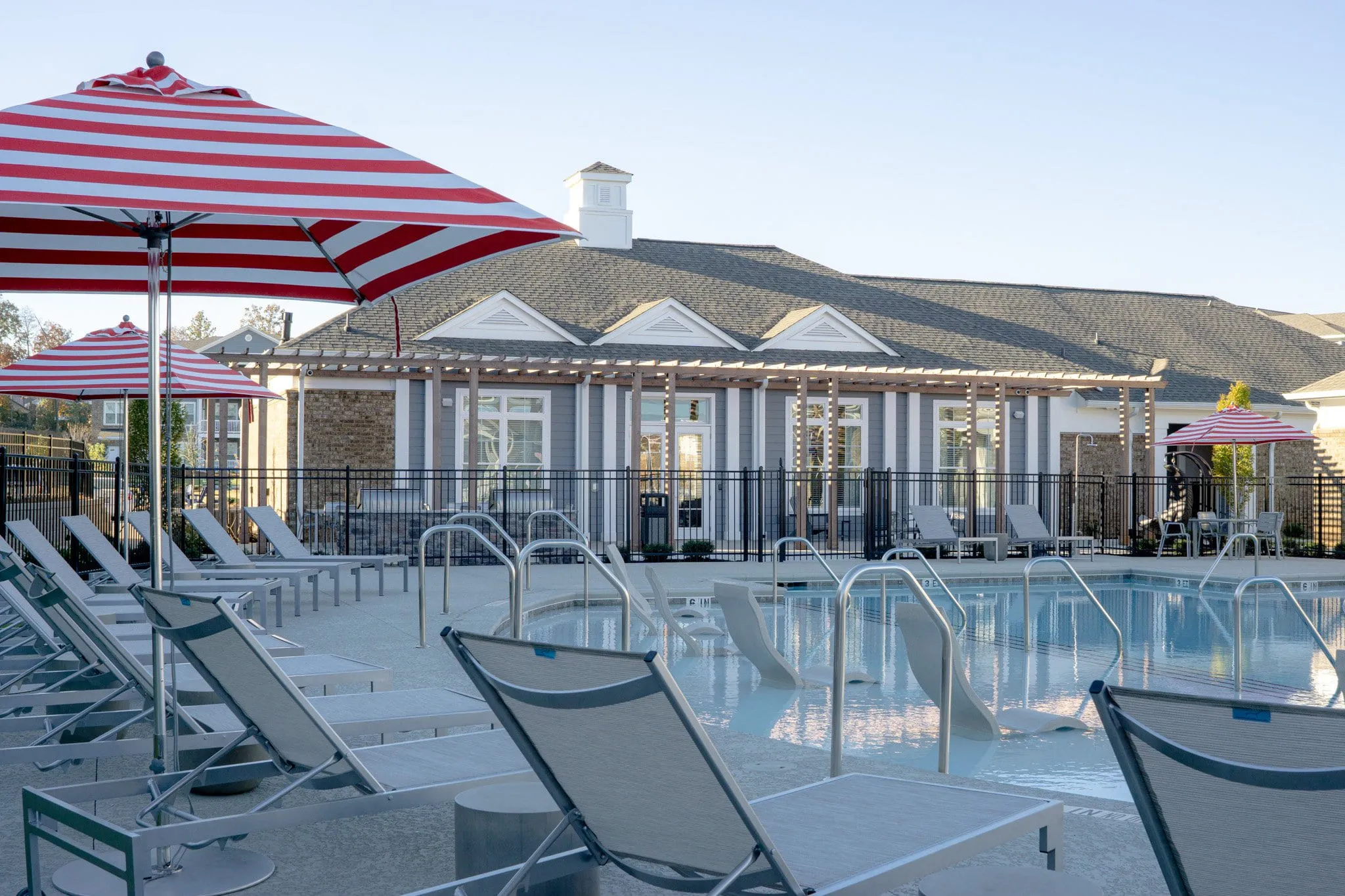 Multifamily community pool with striped umbrellas and loungers in front of the gabled clubhouse