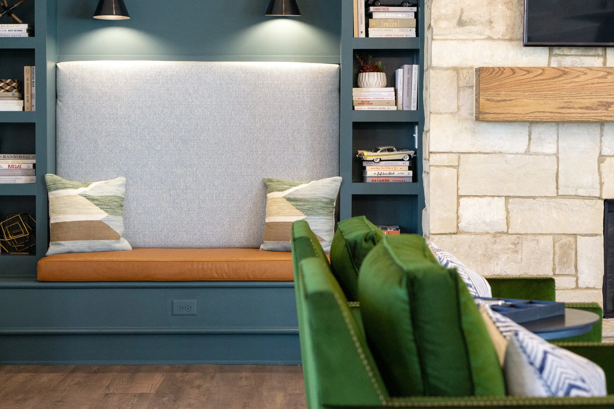 Multifamily amenity clubroom bench nook with an upholstered back between teal shelving and a stone chimney breast