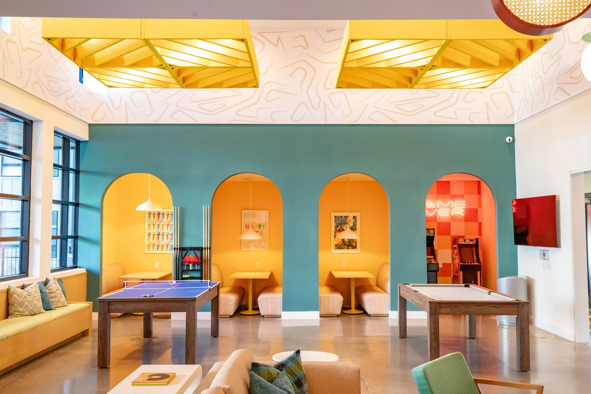 Student housing amenity game room with a ping pong table, shuffleboard and arched yellow and orange booth seating against a teal wall