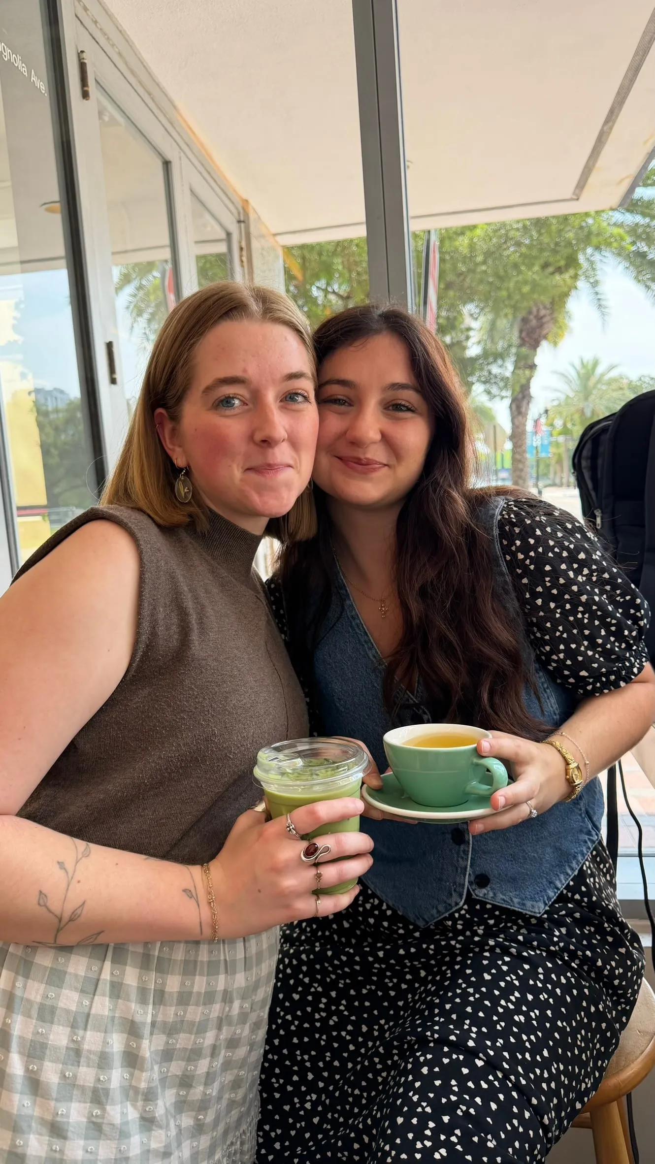 Two colleagues cheek to cheek holding coffee cups in a bright, window-lined room