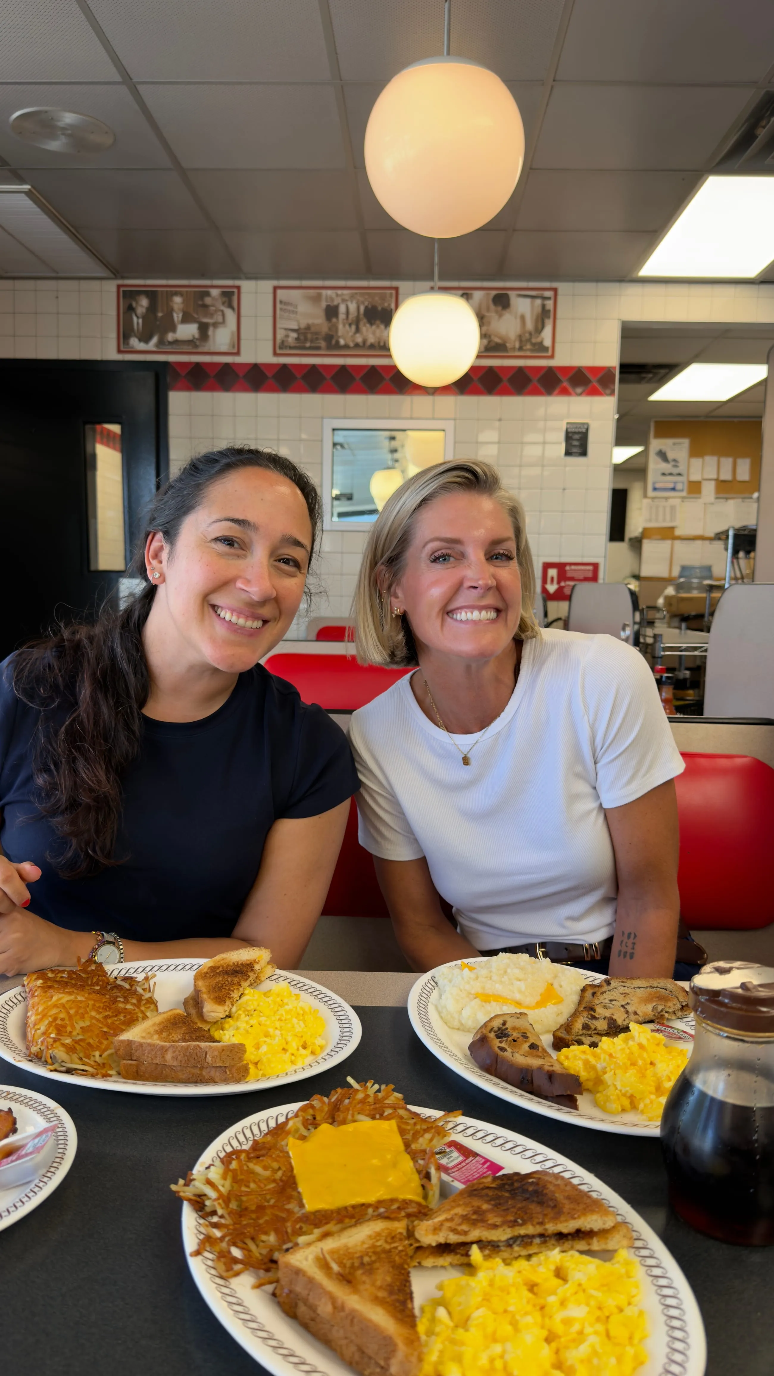 Two colleagues at a diner booth with plates of eggs, hash browns and toast under globe pendant lights