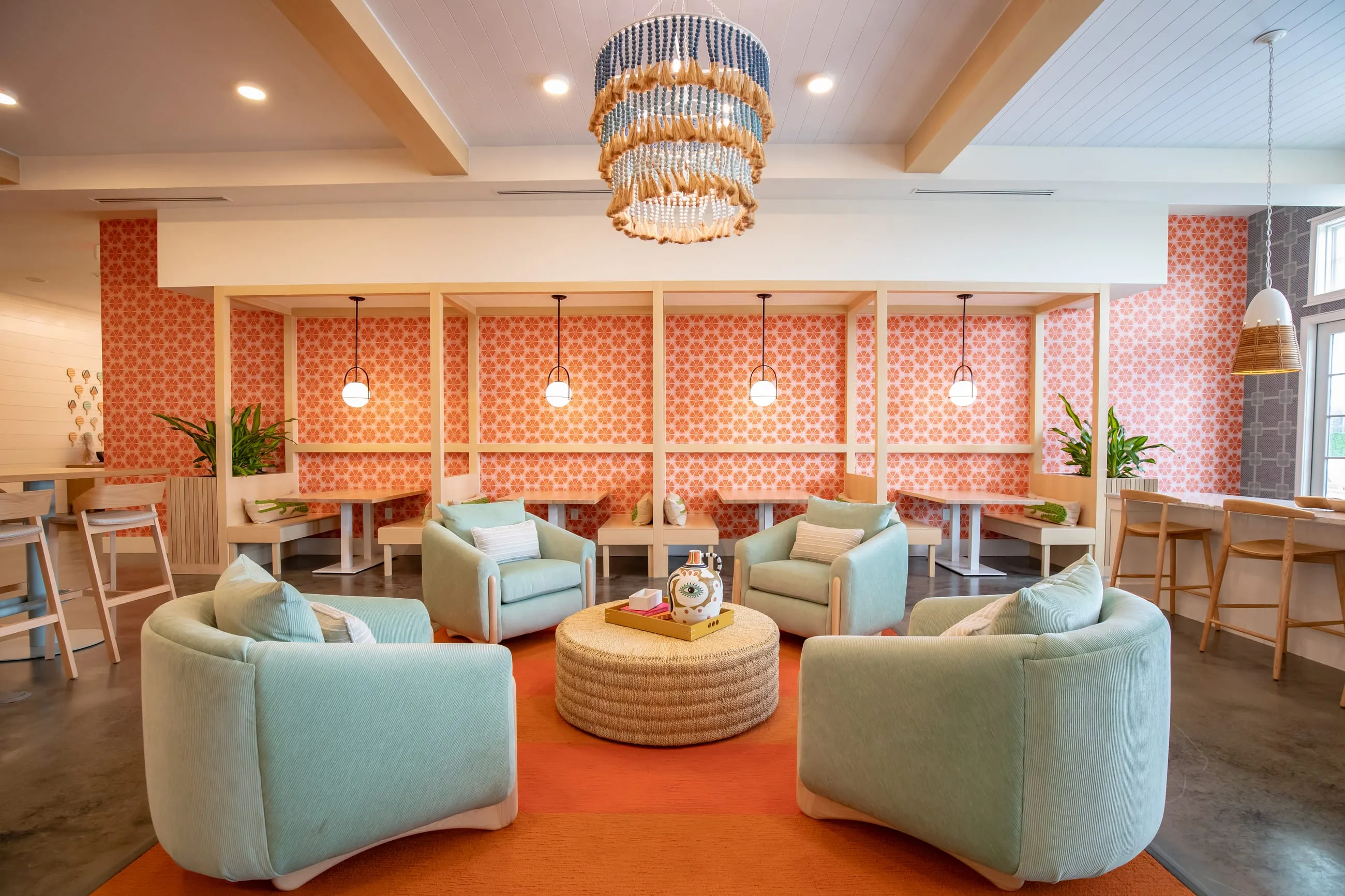 Lounge with coral patterned wallpaper, mint velvet swivel chairs around a round ottoman and a brass chandelier over an orange rug