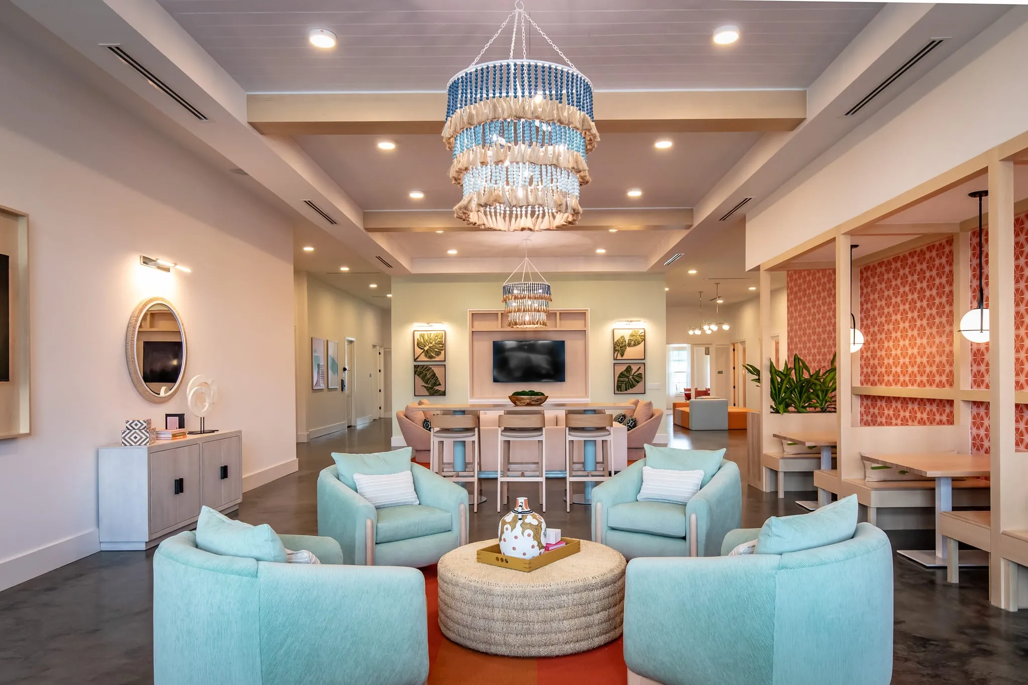 Multifamily amenity clubhouse lounge with mint swivel chairs around a rattan ottoman beneath beaded chandeliers