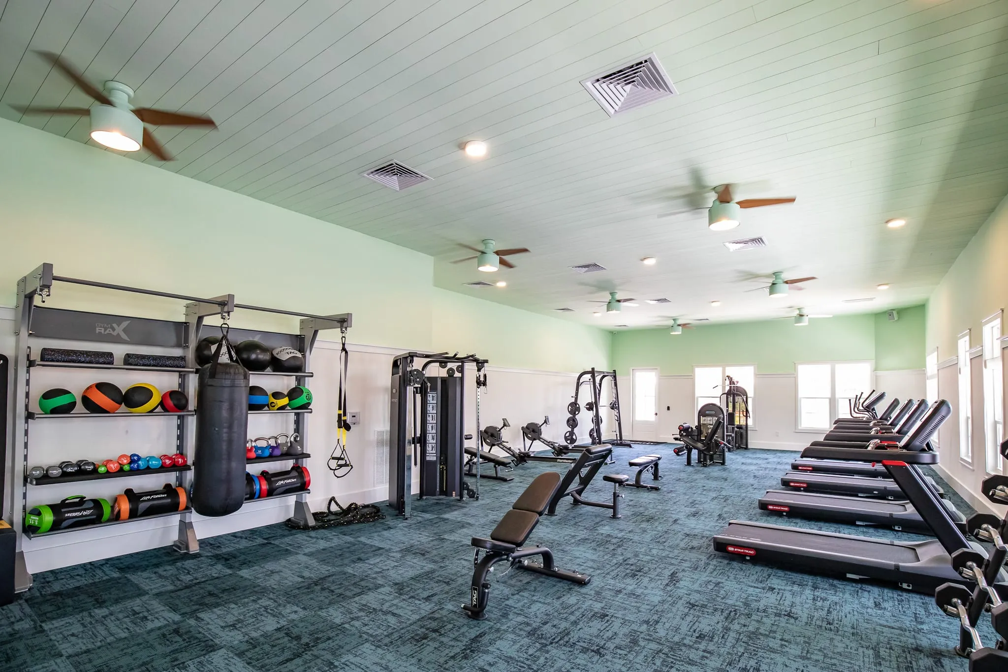 Multifamily amenity fitness center with treadmills and free weights under mint green shiplap and ceiling fans