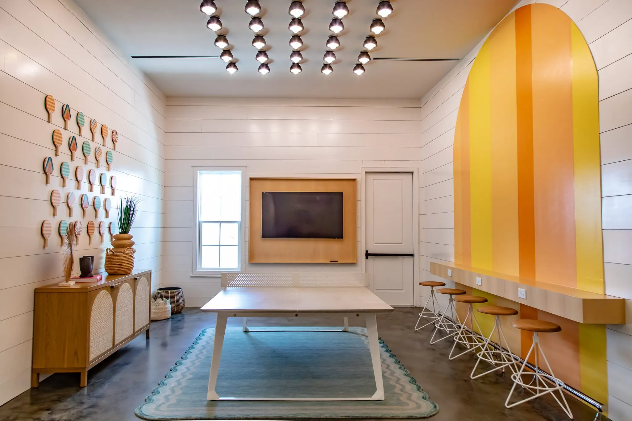 Multifamily amenity game room with a wall of vintage ping pong paddles facing a yellow and orange striped arch