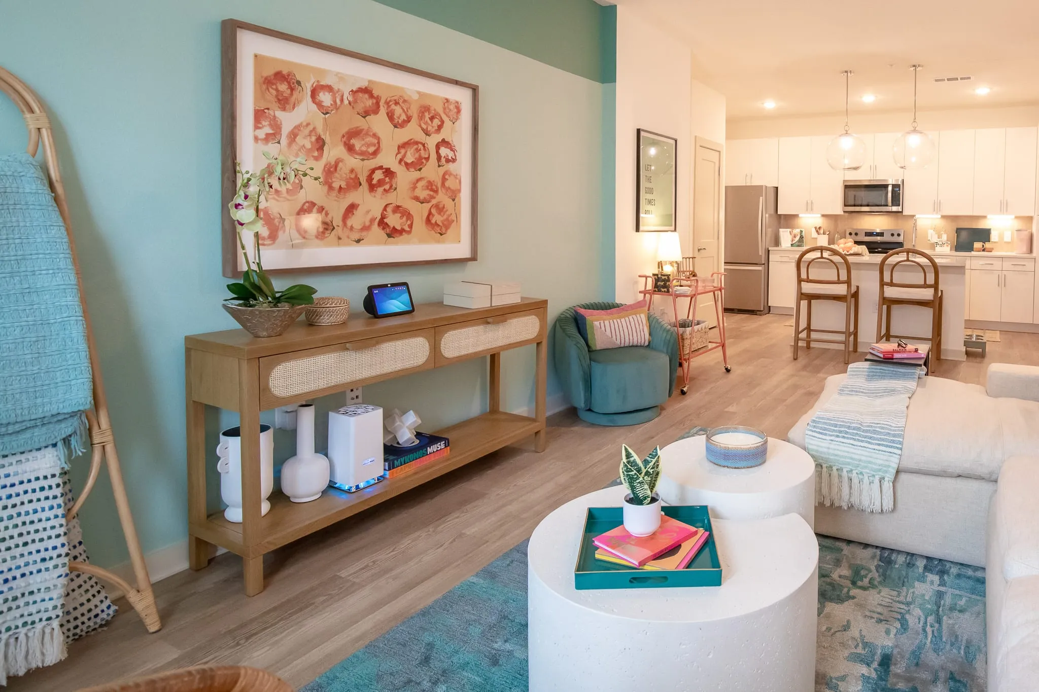Multifamily model apartment living room with a rattan console and teal wall, the kitchen beyond
