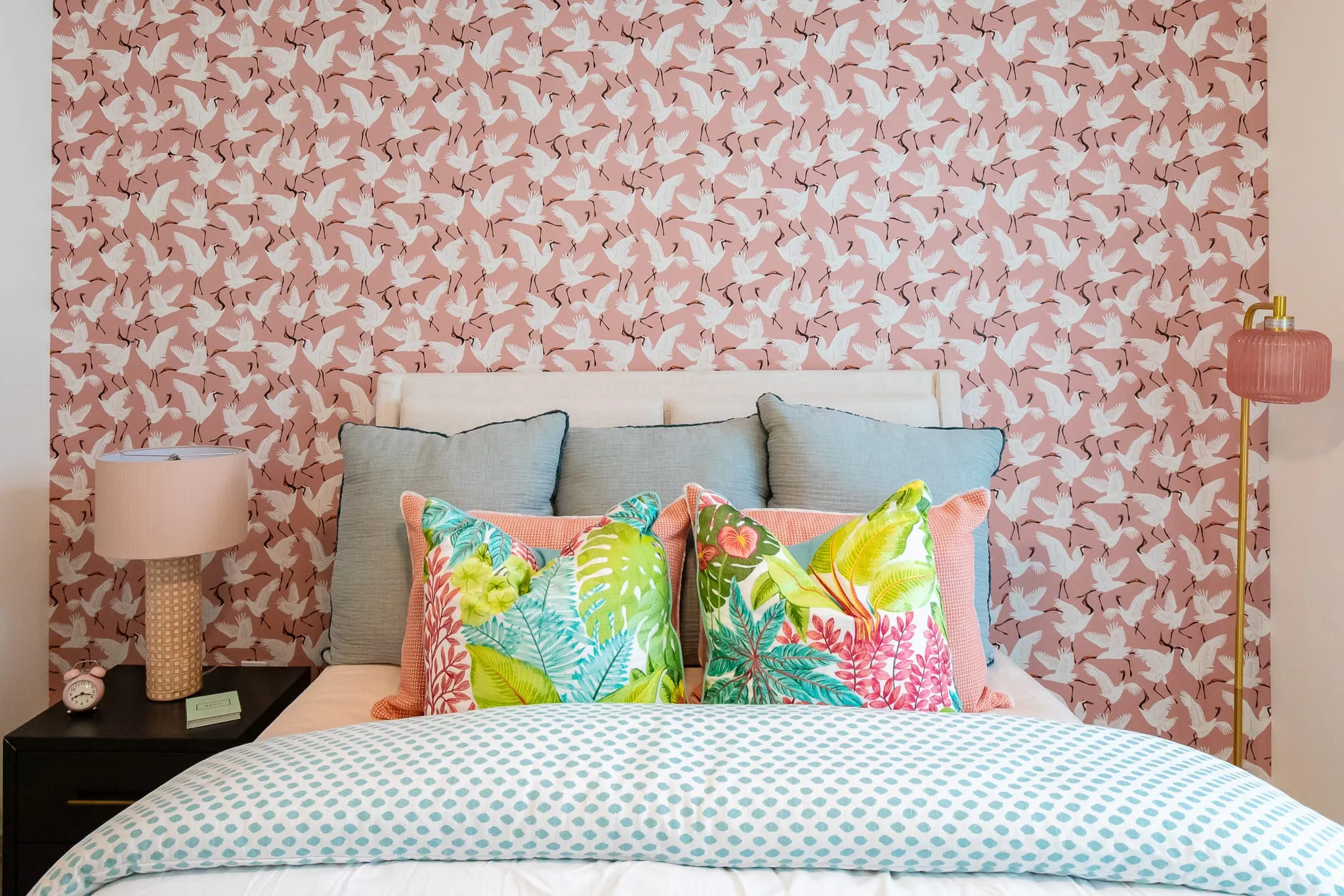 Multifamily model apartment bedroom with pink crane wallpaper behind tropical print pillows on mint quilted bedding