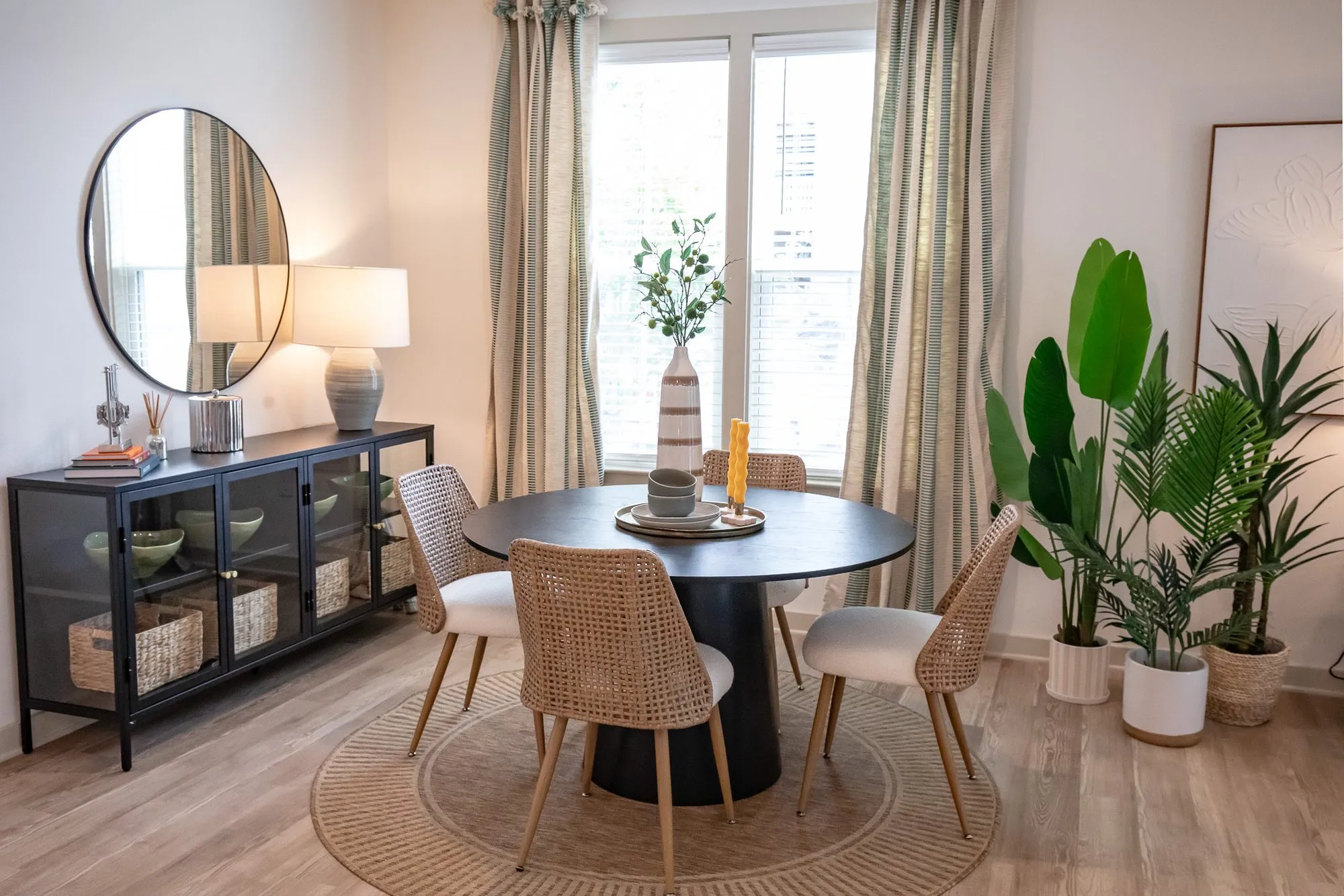 Multifamily model apartment dining area with a round black table, cane back chairs and a jute rug below a round mirror