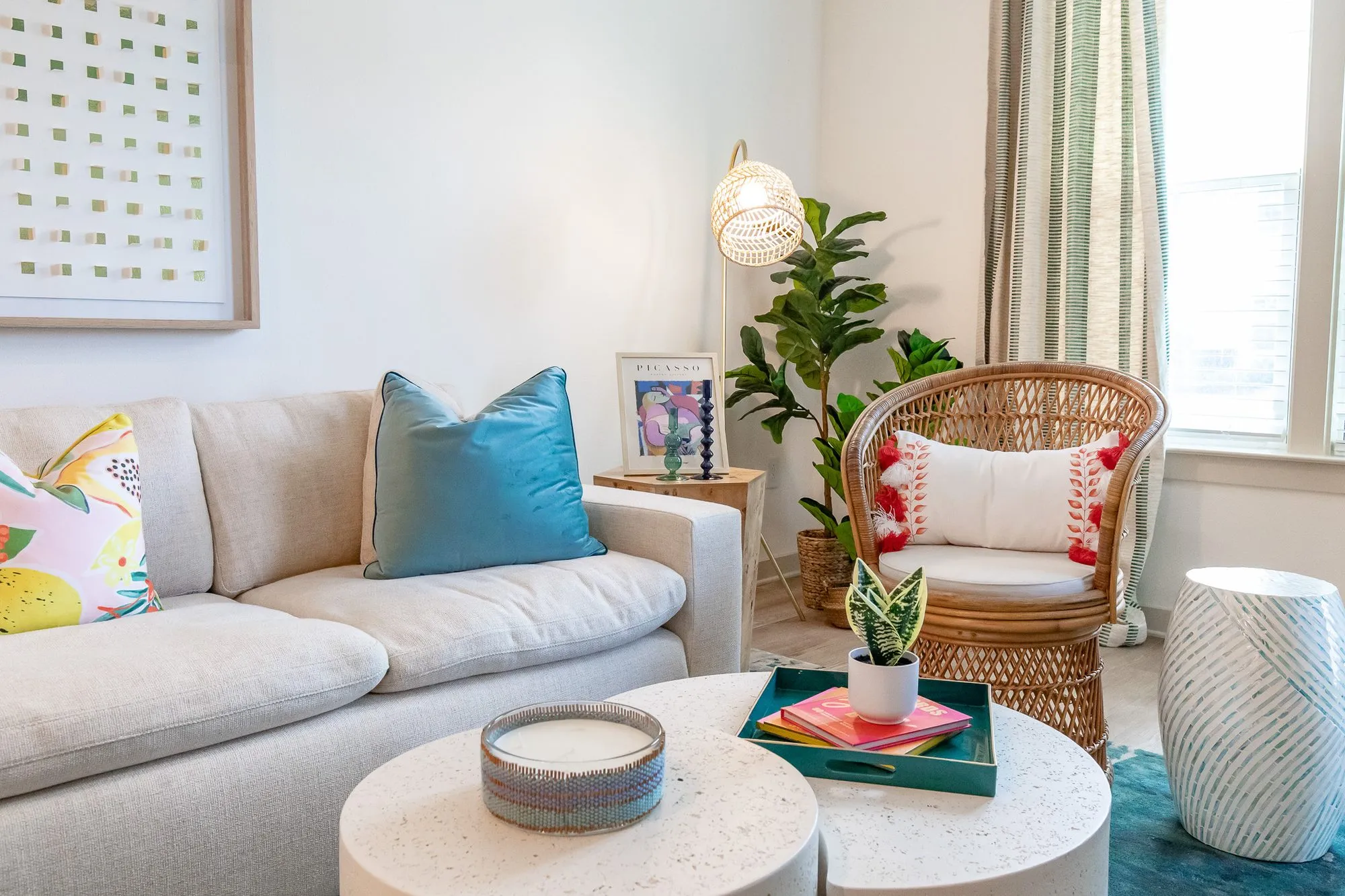 Multifamily model apartment living room with a cream sofa, rattan peacock chair, white drum tables and a fiddle leaf fig