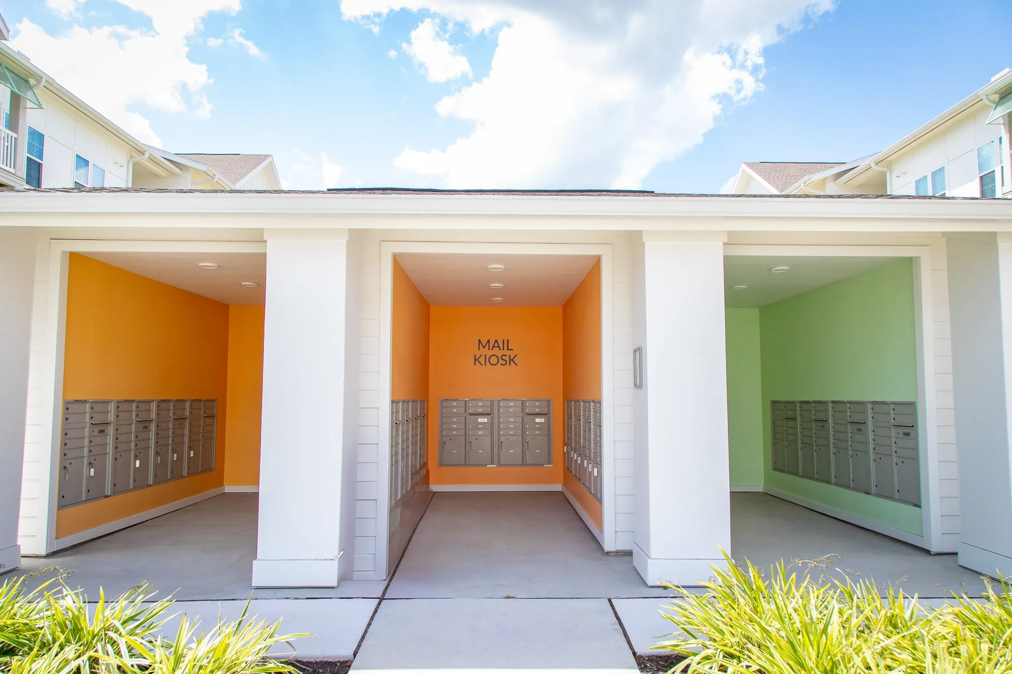 Multifamily amenity mail kiosk with white columns framing open bays painted orange and green, lined with mailboxes