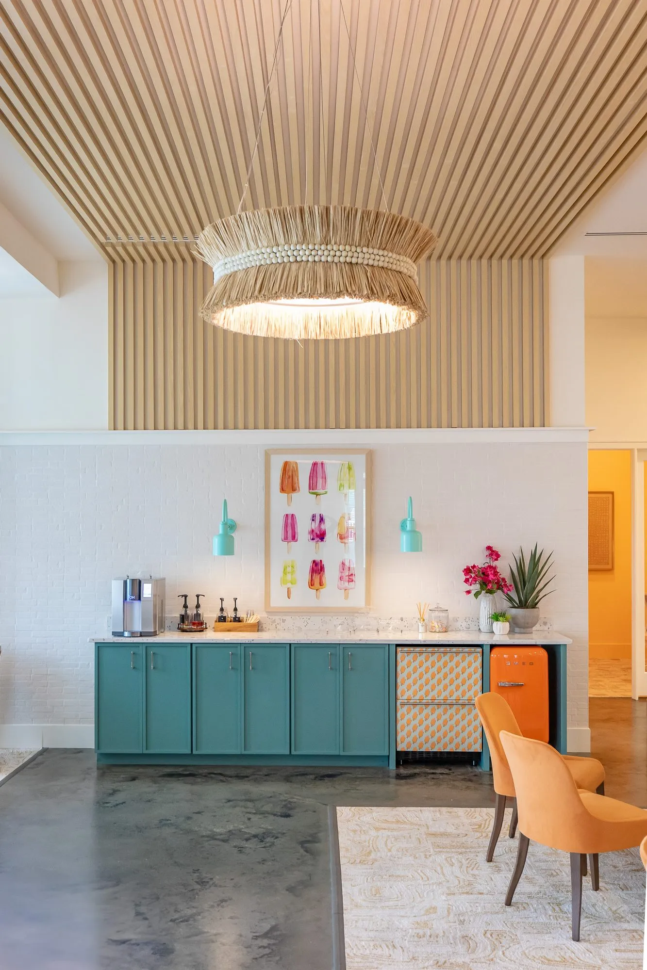 Multifamily amenity coffee bar cabinet in teal with a popsicle print below a slatted wood ceiling and fringed rattan pendant