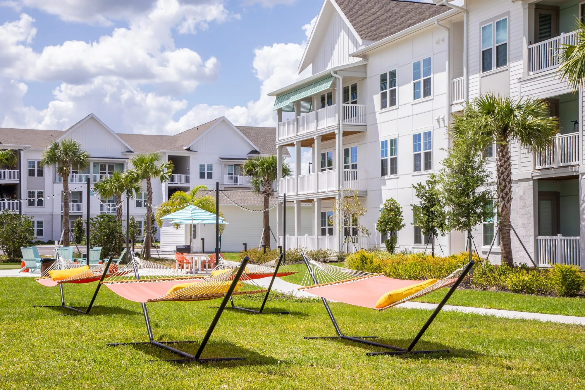 Multifamily amenity lawn with orange and yellow hammocks on black stands between white apartment buildings and palms