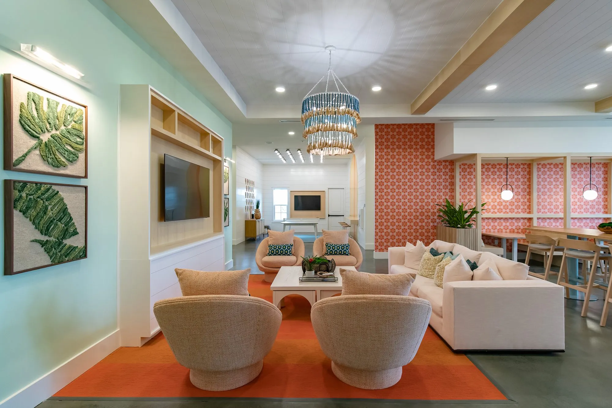Multifamily amenity clubroom with mint walls and leaf art, rattan swivel chairs on an orange rug and coral booths