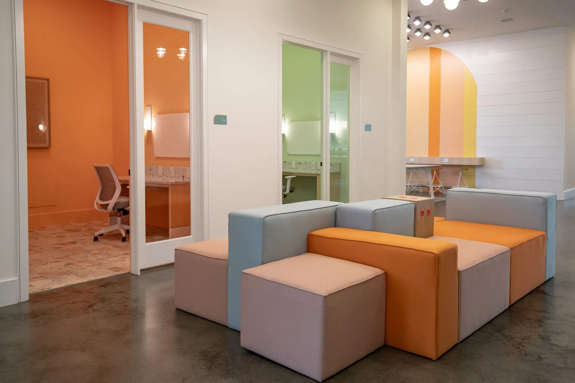 Multifamily interior detail: modular cube seating in orange, blue and blush beside an open door to an orange office