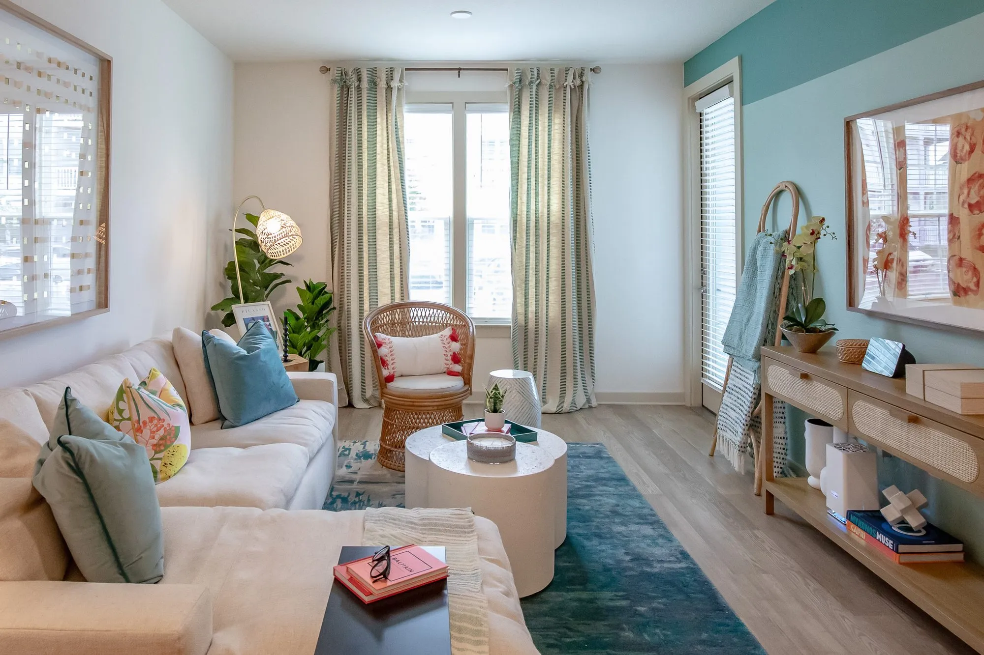 Multifamily model apartment living room with a cream sectional, rattan chair, white drum tables, a teal rug and accent wall