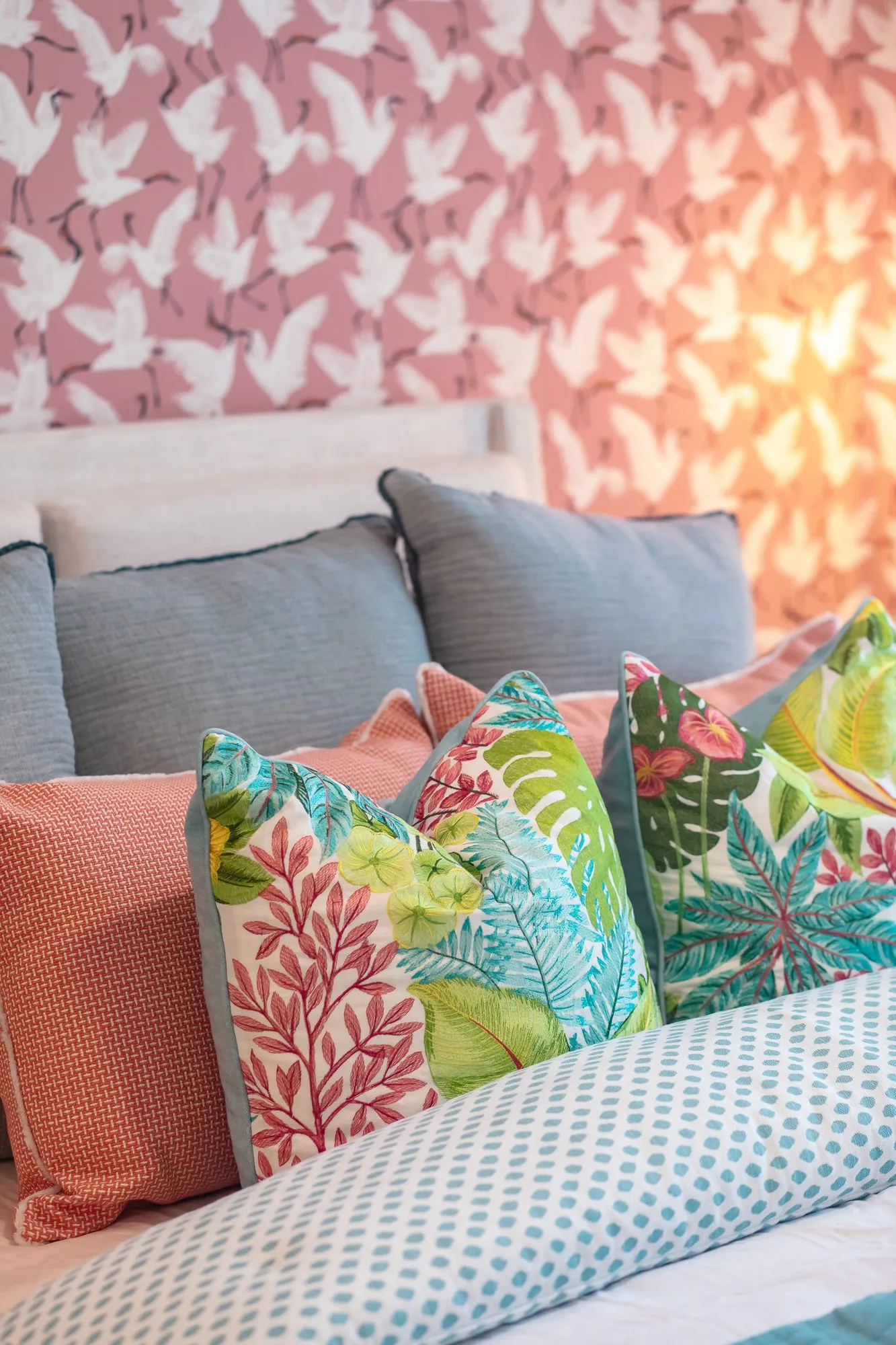 Multifamily apartment bedroom detail: tropical print and coral pillows on a bed against pink bird wallpaper